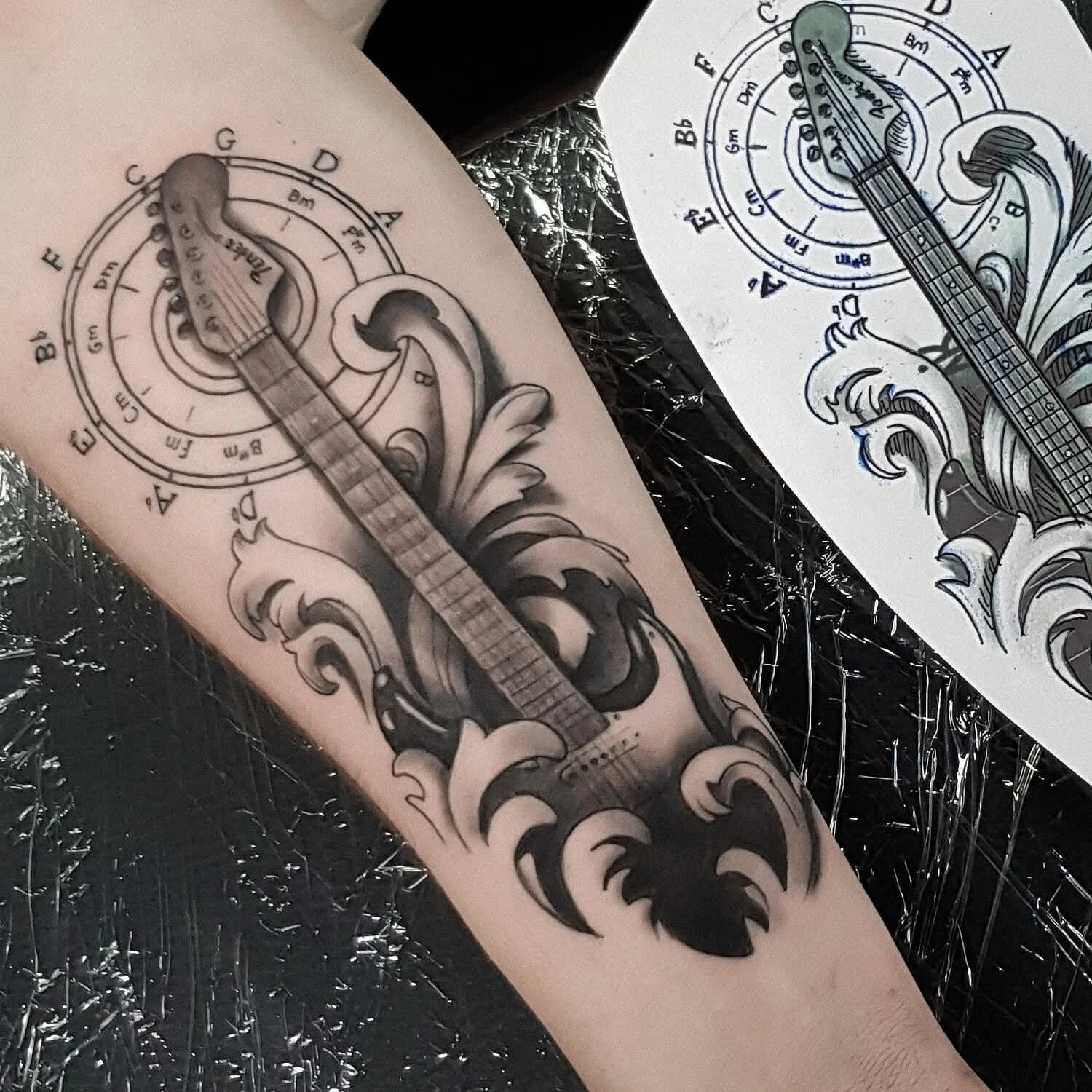 Schwarzes und graues Tattoo eines akustischen Gitarrenkorpus  auf einem Unterarm