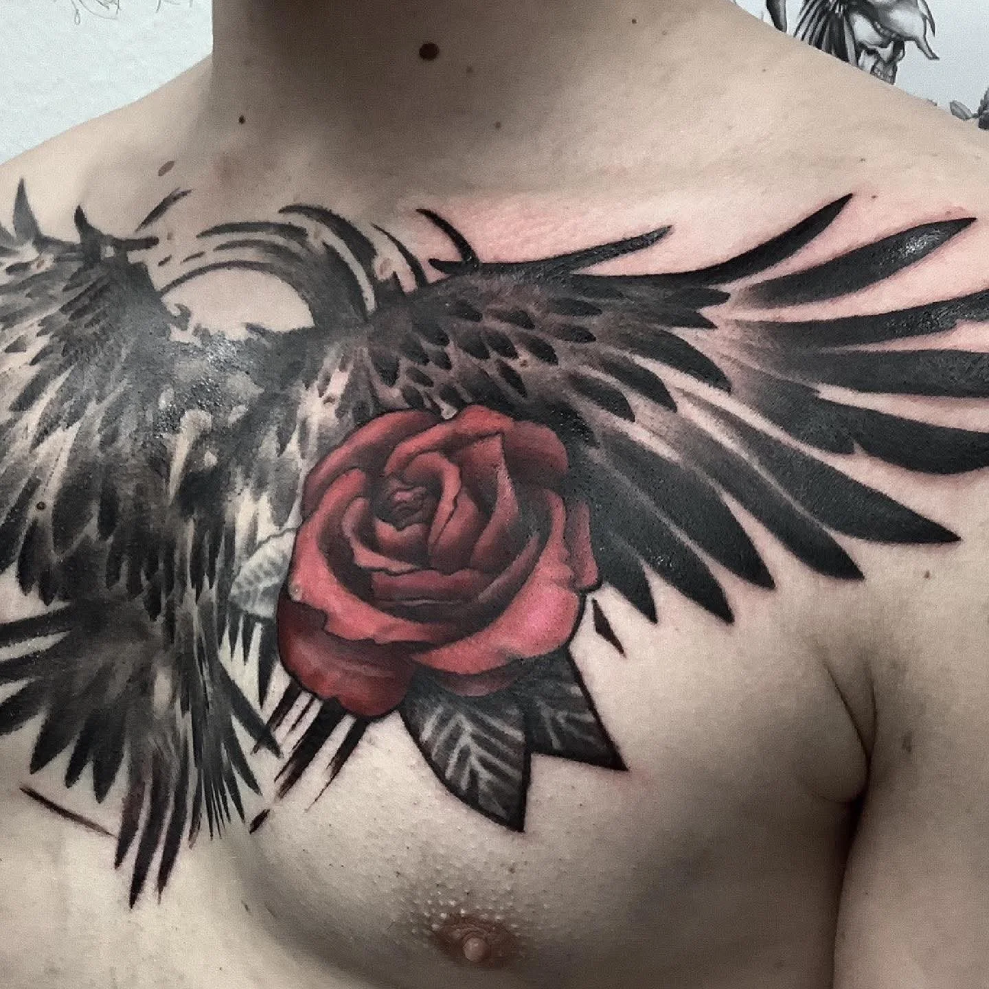 Tattoo eines roten Rosen mit schwarzen Flügeln auf der Brust eines Menschen.