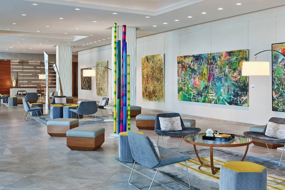 Sarasota Motor Club - premium car service sarasota - Modern hotel lobby with colorful artwork on white walls, contemporary chairs, ottomans, and tables, and tall, vibrant glass sculpture in the center.