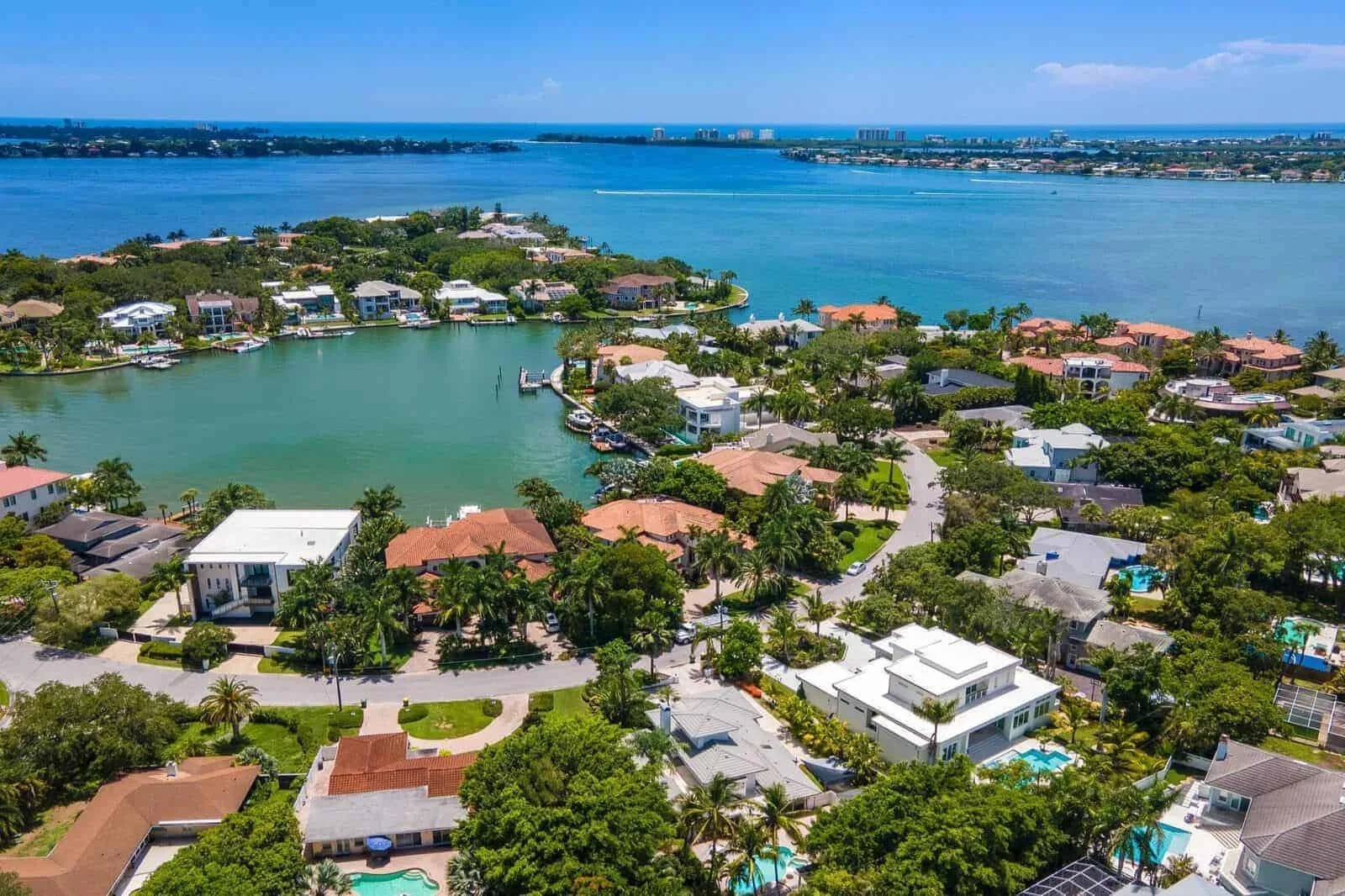 Sarasota Motor Club - Sports Car Rental Sarasota FL - Aerial view of a coastal neighborhood with waterfront houses, a large body of water, and lush greenery under a partly cloudy sky.