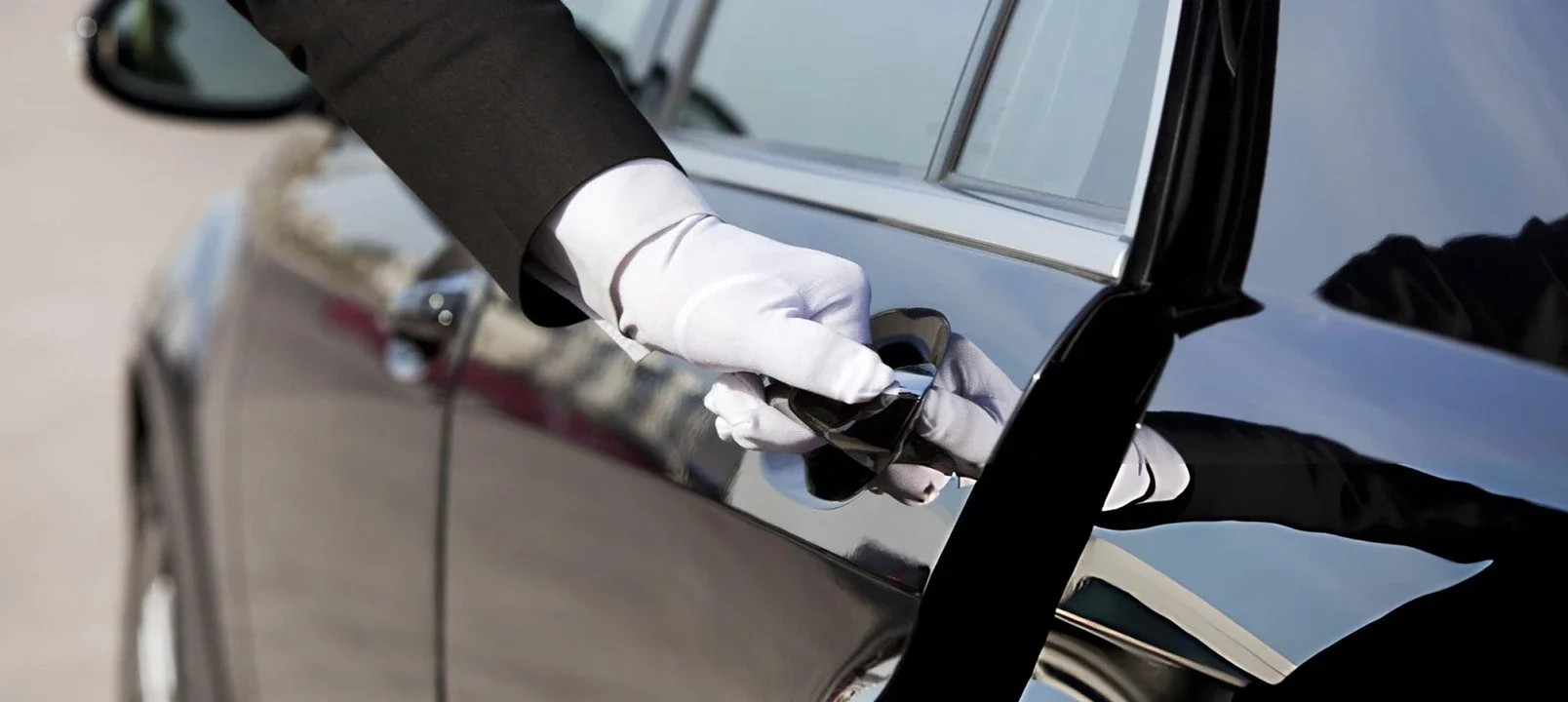 Sarasota Motor Club - Sports Car Rental Sarasota FL - A person in a tuxedo with white gloves is opening the door of a black luxury car.