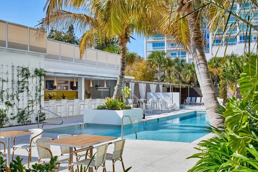 Luxury outdoor pool area with lounge chairs, tables, palm trees, and modern cabanas at a hotel or resort.