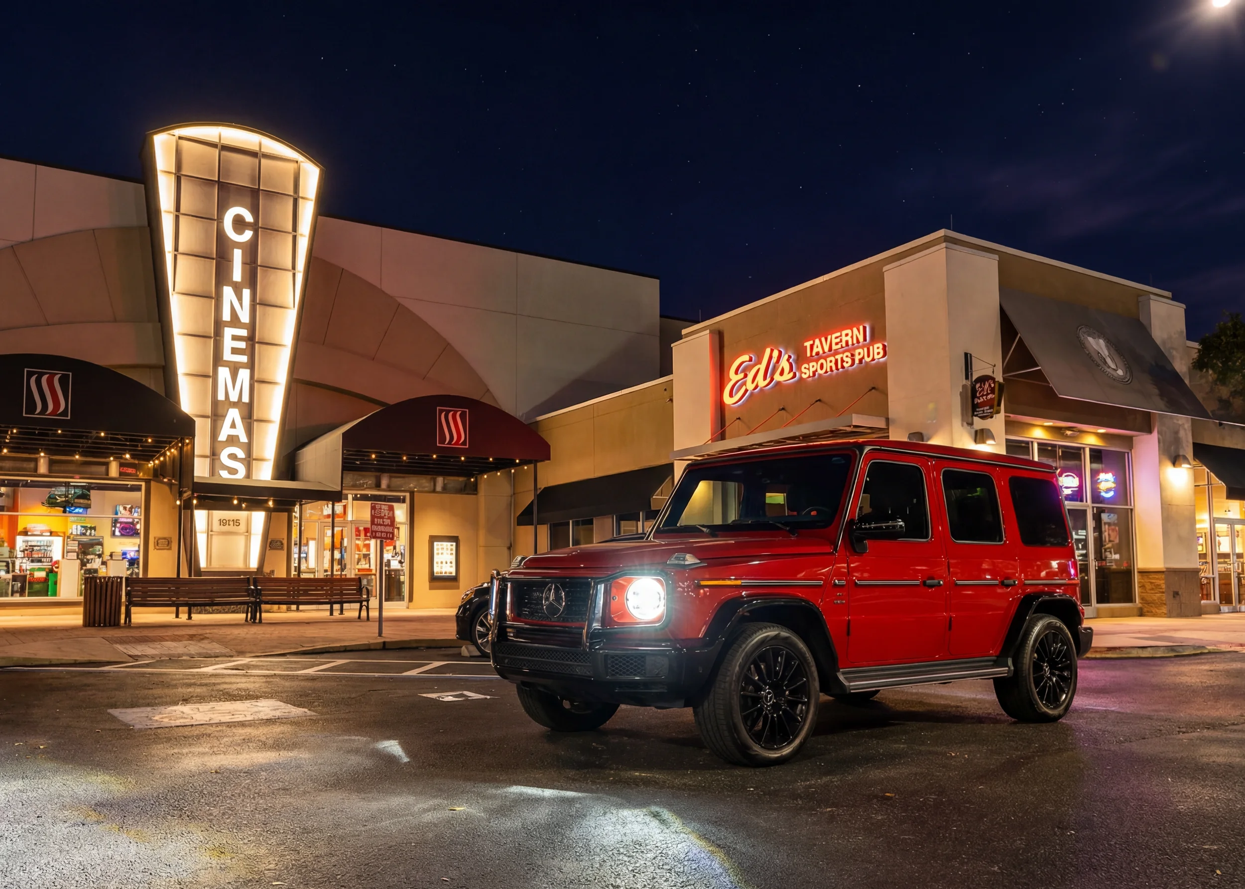 Sarasota Motor Club - Sarasota exotic car rental - A red Mercedes-Benz G-Class SUV is parked in the foreground. Nighttime scene of a parking lot in front of a movie theater with a large illuminated sign that reads 'CINEMAS'.