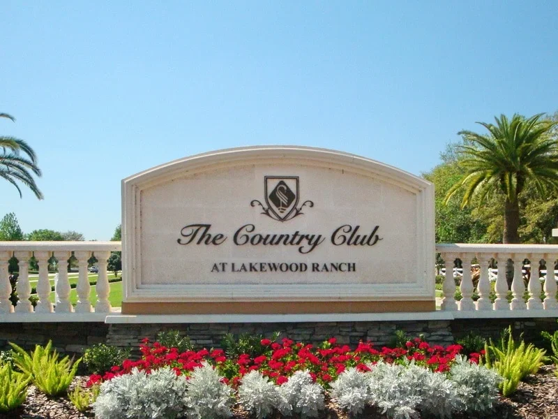 Sarasota Motor Club - Premium Car Service Sarasota - Sign for The Country Club at Lakewood Ranch surrounded by colorful flowers and palm trees.