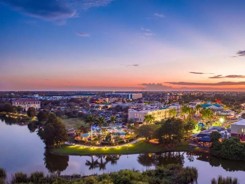 Sarasota Motor Club - Premium Car Service Sarasota - A scenic evening view of a city with colorful sunset sky, water bodies, trees, and well-lit buildings.