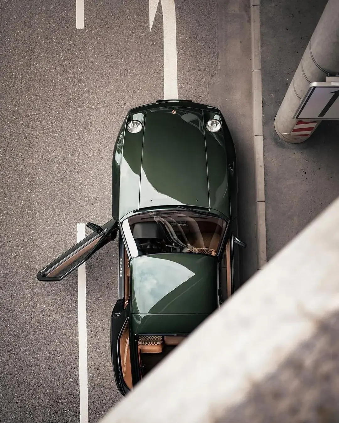 Sarasota Motor Club - Exotic Car Rental Sarasota - A dark green car with its driver's side door open, parked in a parking lot next to a concrete wall and a parking sign.