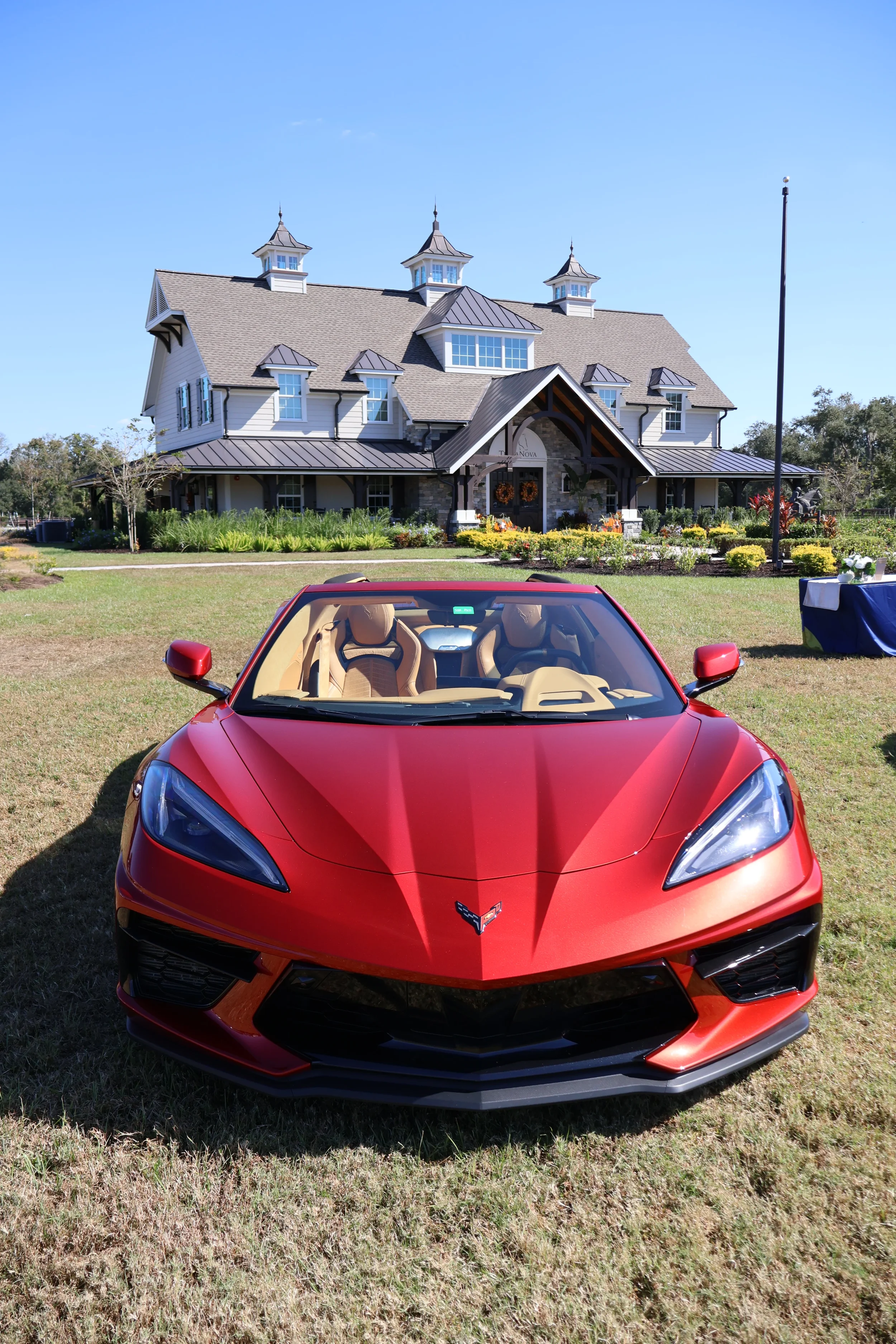 Sarasota Motor Club - exotic car rental sarasota florida - Red Corvette parked on grass in front of a large, elegant house with a garden and blue sky.