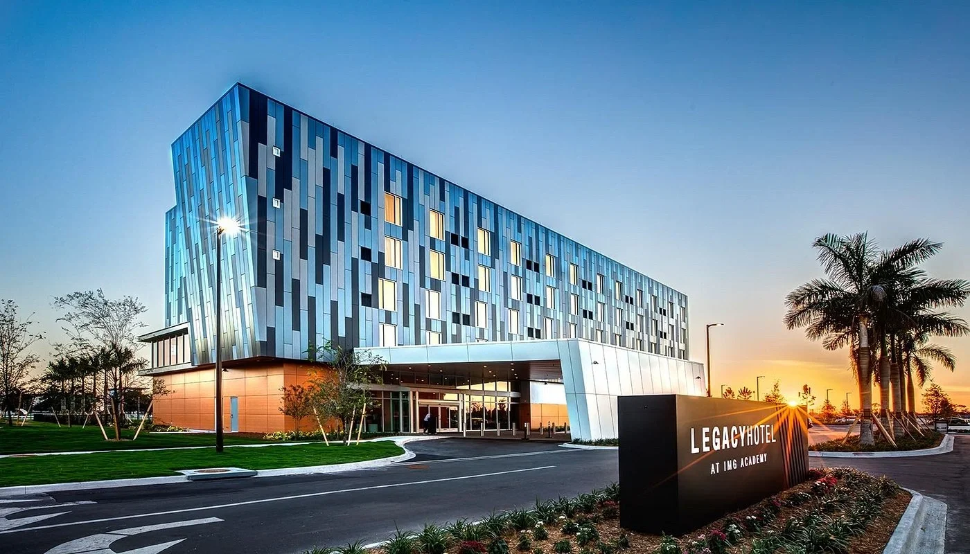 Sarasota Motor Club - Exotic Car Rental Sarasota Florida - Modern hotel building during sunset with a sign that reads 'LEGACY HOTEL AT I MG ACADEMY' in front.