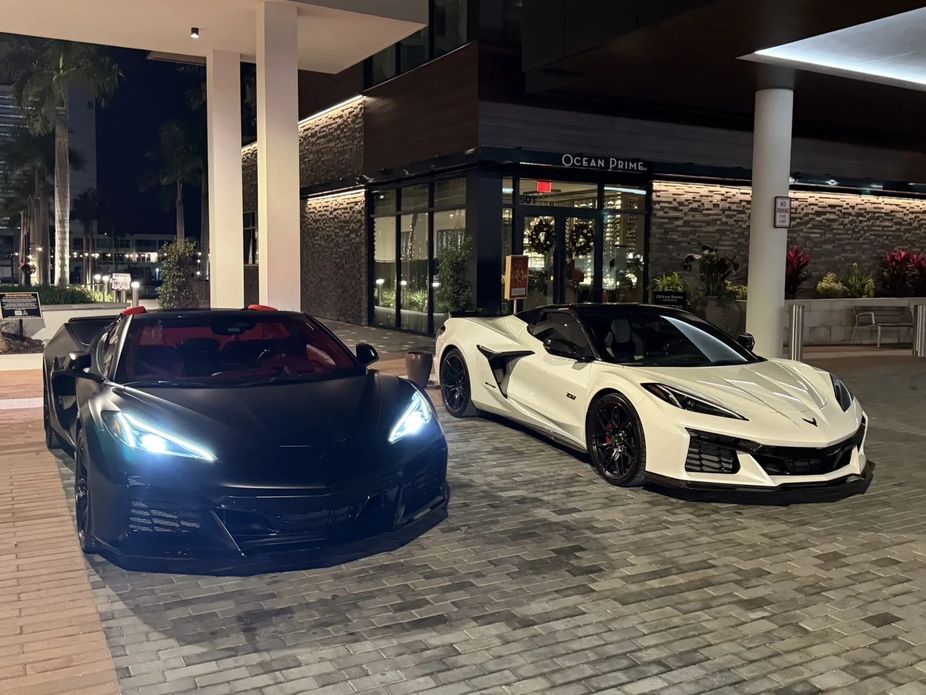 Sarasota Motor Club - sports car rental sarasota fl - Two sports cars, a black one on the left and a white one on the right, parked outside a building at night.