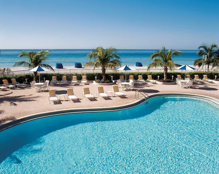 Sarasota Motor Club - Lido Beach Resort exotic car rental - Aerial view of a luxury beachfront resort with multiple swimming pools, palm trees, lounge chairs, and direct access to a sandy beach and blue ocean.