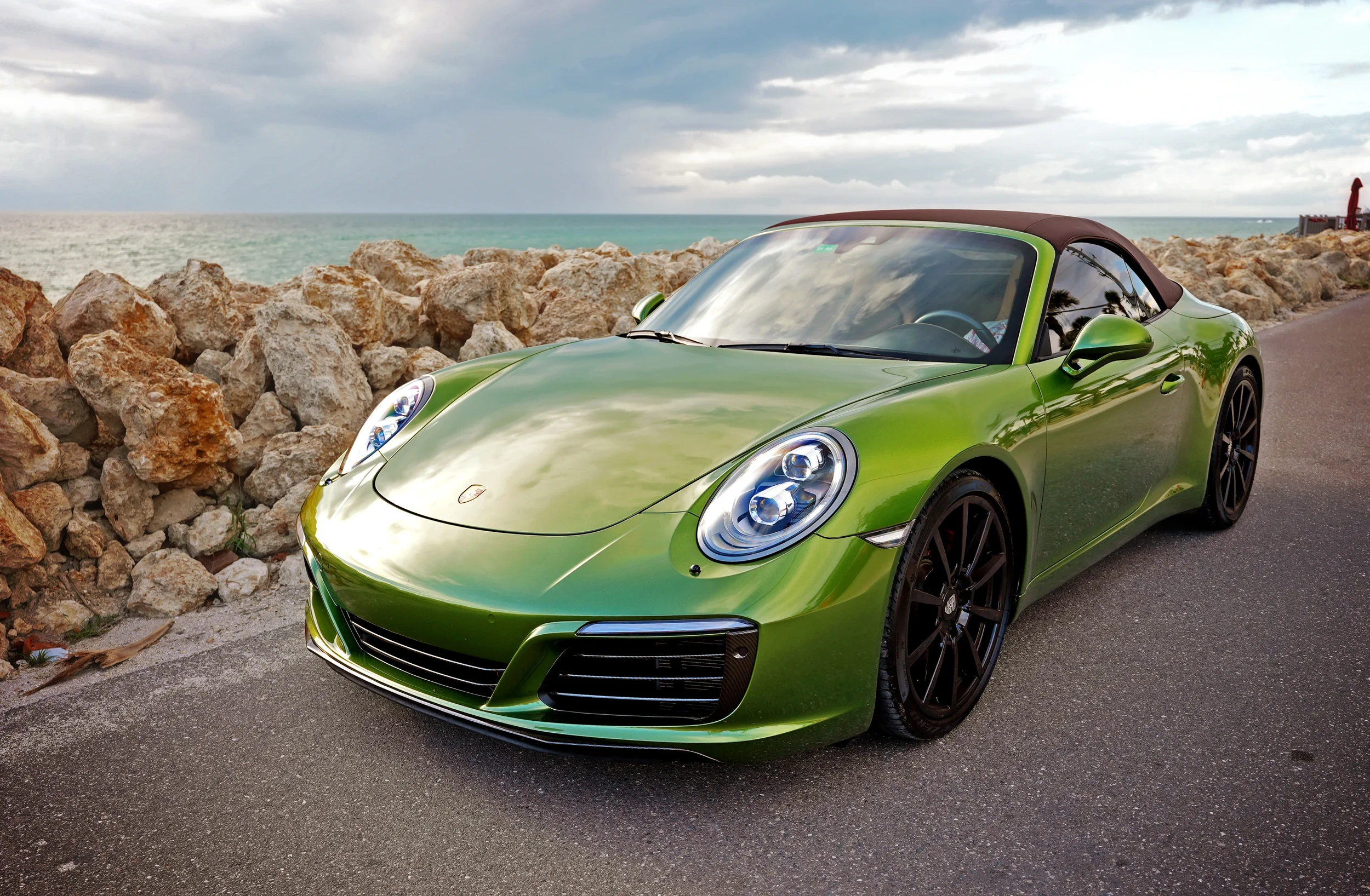 Sarasota Motor Club - Premium Car Service Sarasota - A shiny green Porsche 911 GT3 car parked on the side of a coastal road with rocks and the ocean in the background.
