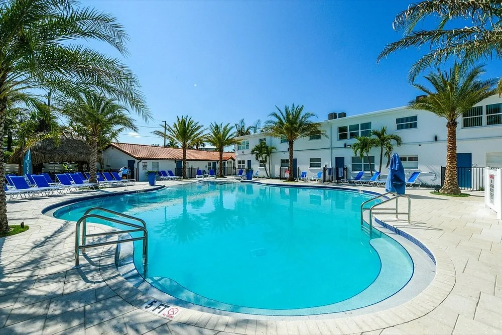 Sarasota Motor Club - Premium Car Service Sarasota - Outdoor hotel swimming pool with blue lounge chairs and palm trees, sunny day.