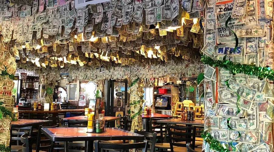 Interior of a restaurant decorated with hanging and wrapped dollar bills, along with green tinsel, creating a money-themed decor.