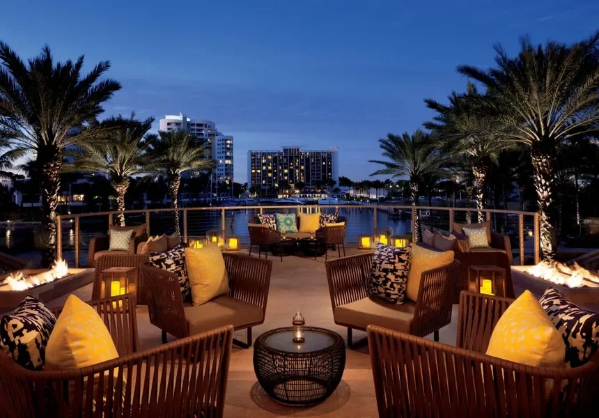 Sarasota Motor Club - Ritz Carlton exotic car rental - A tropical hotel pool area with palm trees, lounge chairs with umbrellas, and cabanas. People are swimming and relaxing on chairs.