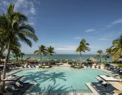 Sarasota Motor Club - Ritz Carlton exotic car rental - Beachside resort pool with palm trees, lounge chairs, and a view of the ocean.