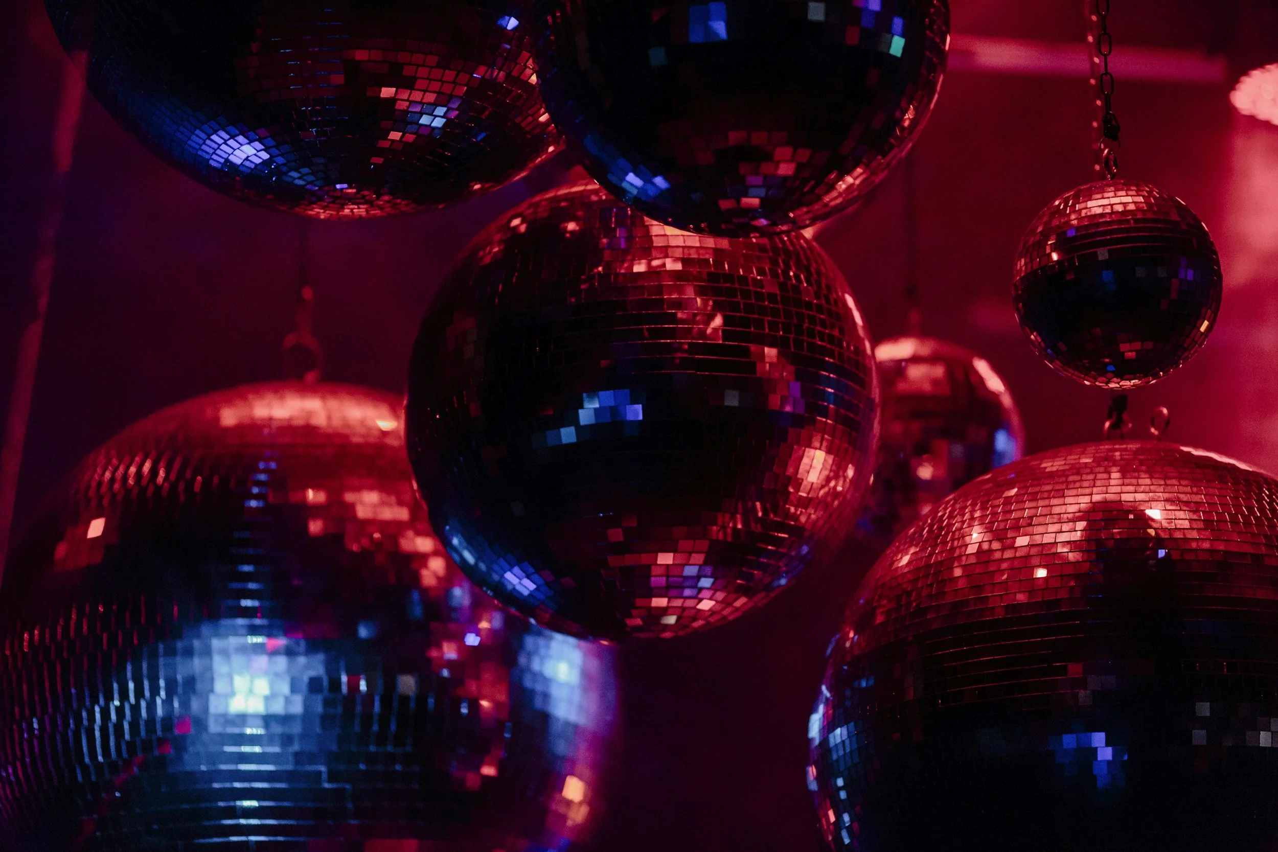 Multiple disco balls in a dark room, reflecting colorful red and blue lights.