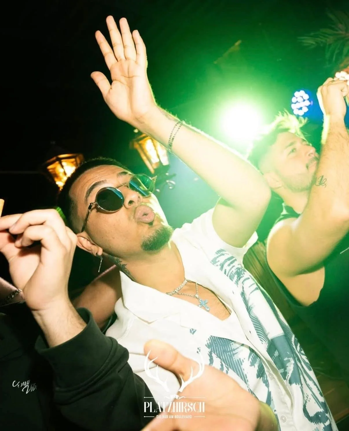 People dancing at a nightclub with green lighting and wearing sunglasses.