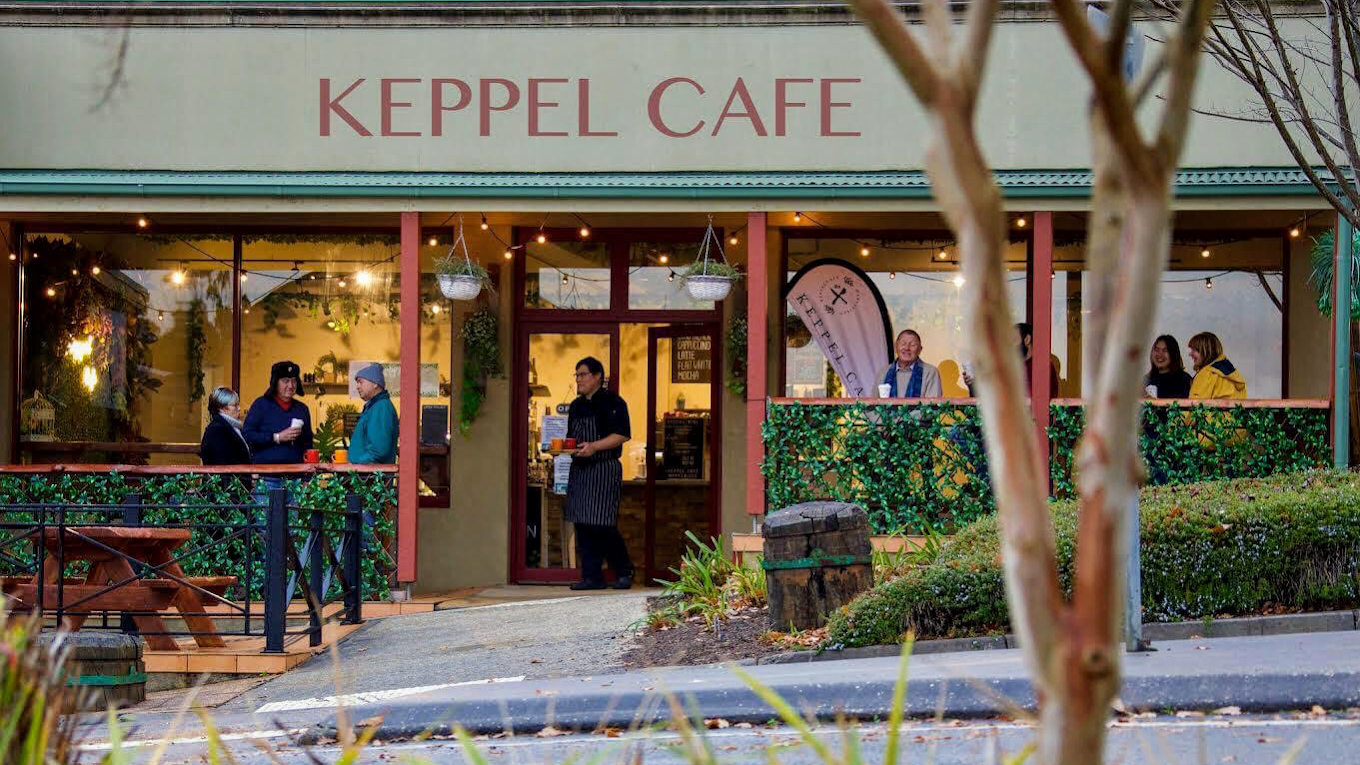 Exterior view of Keppel Cafe with people inside and outside, some talking and servers attending to customers.