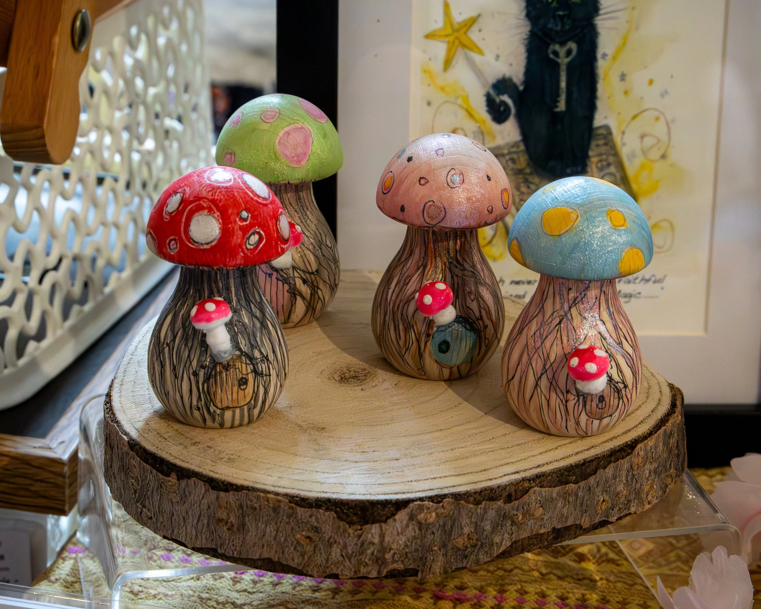 Handmade ceramic mushrooms in red, green, pink, and blue with various dot patterns displayed on a wooden table.