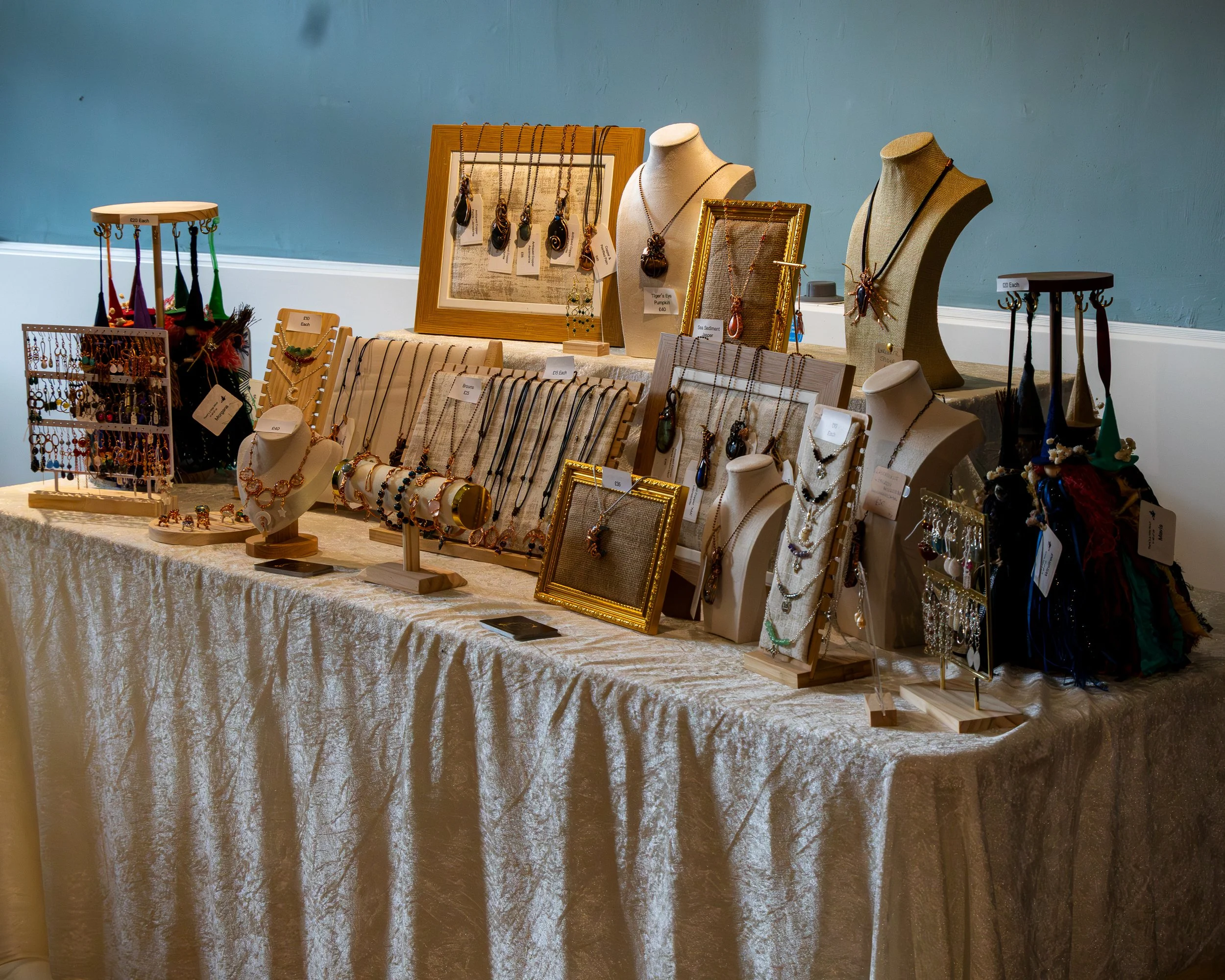 A display of jewelry including necklaces, earrings, and bracelets arranged on bust forms, jewelry stands, and tables at a market or craft fair.