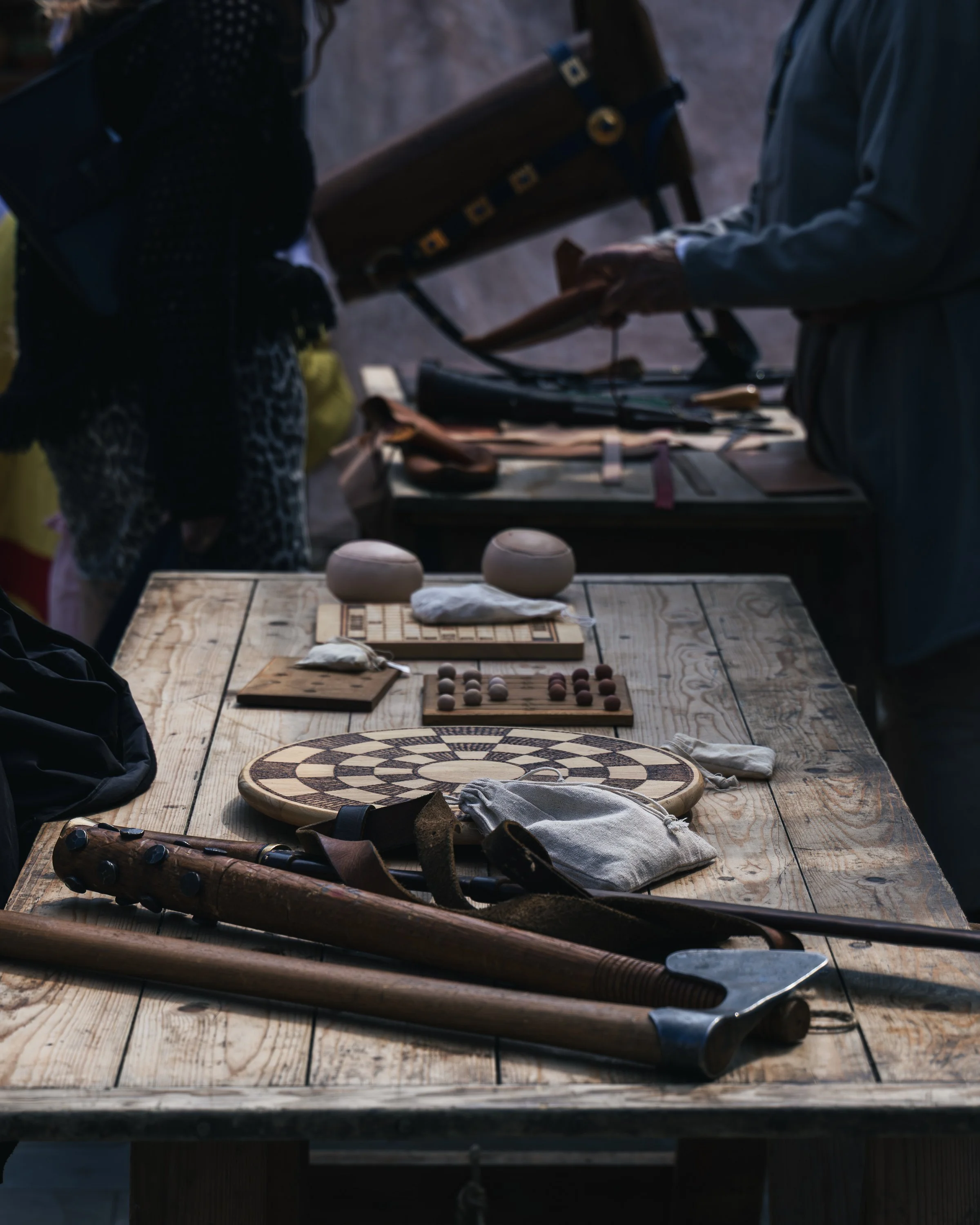 A wooden table with chess pieces, bowls, and various objects, with sports equipment like hockey sticks and an ice skate lying on the table, in a setting that appears to be outdoors or in a garage.