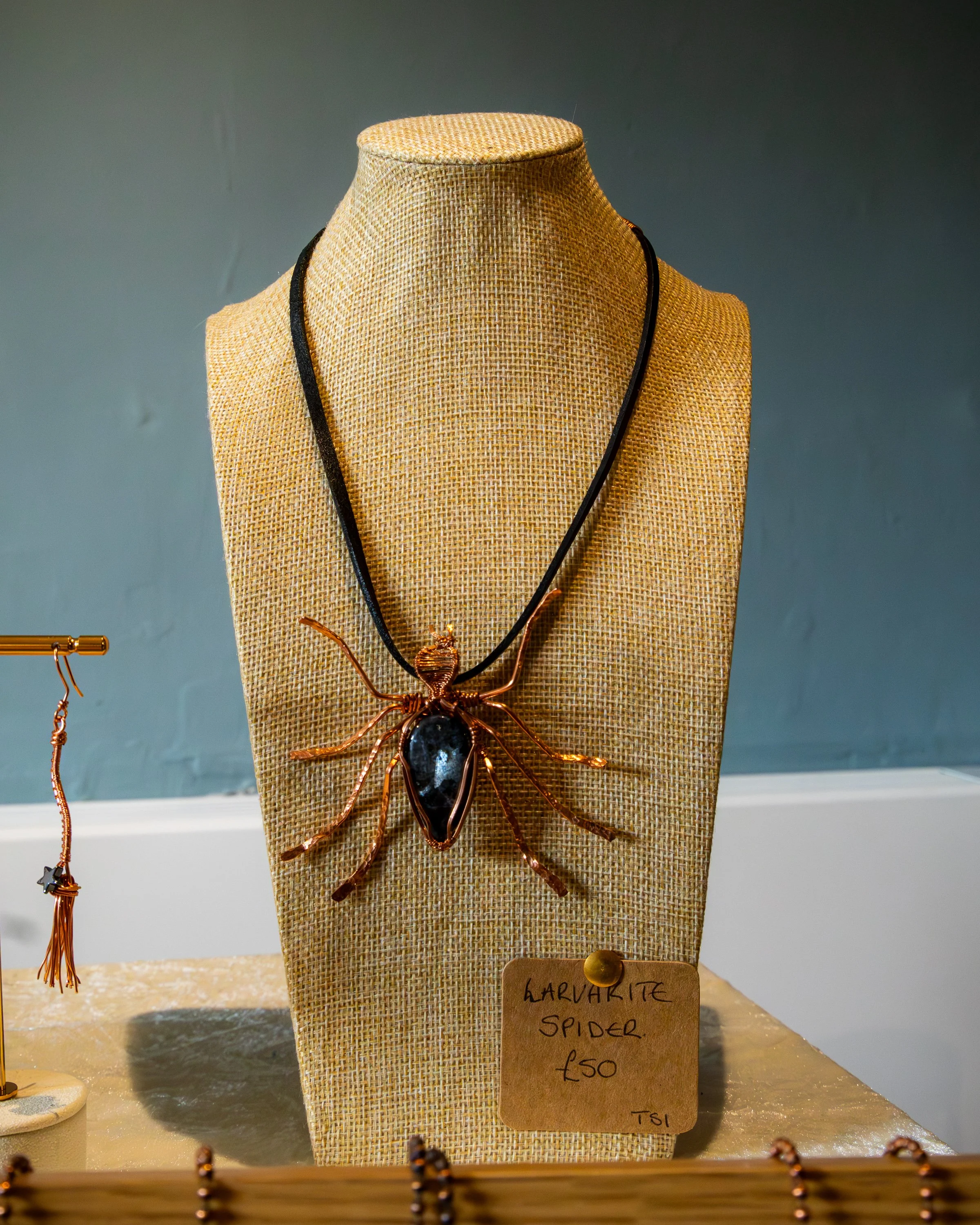 Close-up of a woven jewelry display bust featuring a large copper spider necklace with black gemstone body, labeled 'HARVIKITE SPIDER £50'.