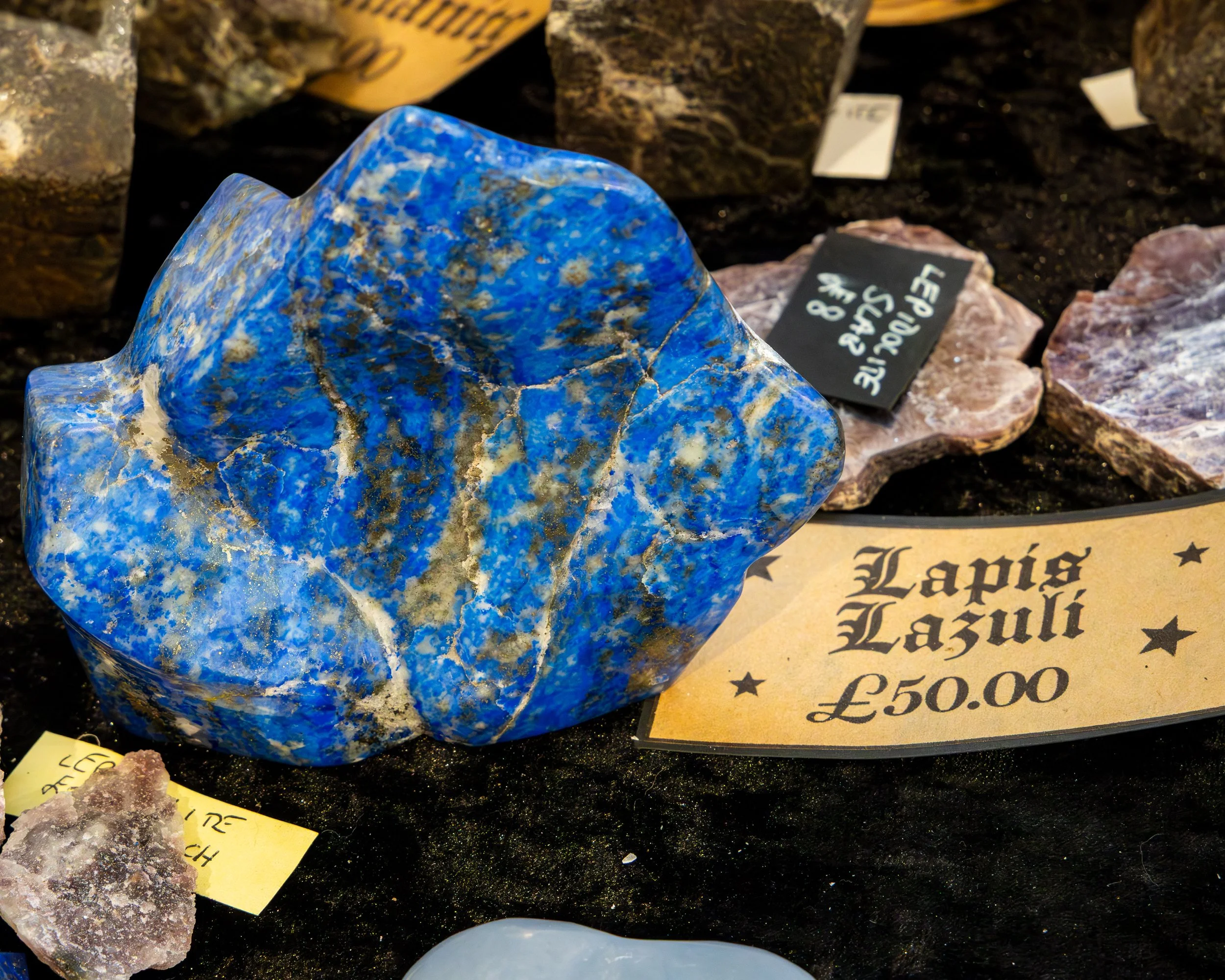 A polished blue mineral sample on display at a market, with a sign indicating its price of £50.00.