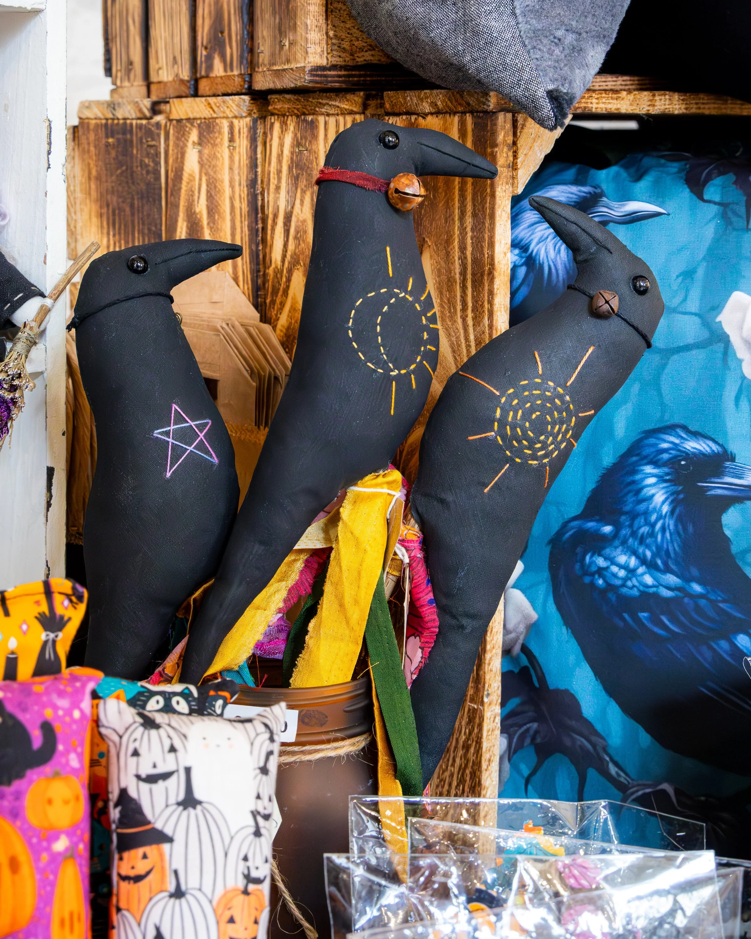 Colorful Halloween-themed fabric and plush decorations, including black cat and pumpkin designs, displayed on a retail shelf.
