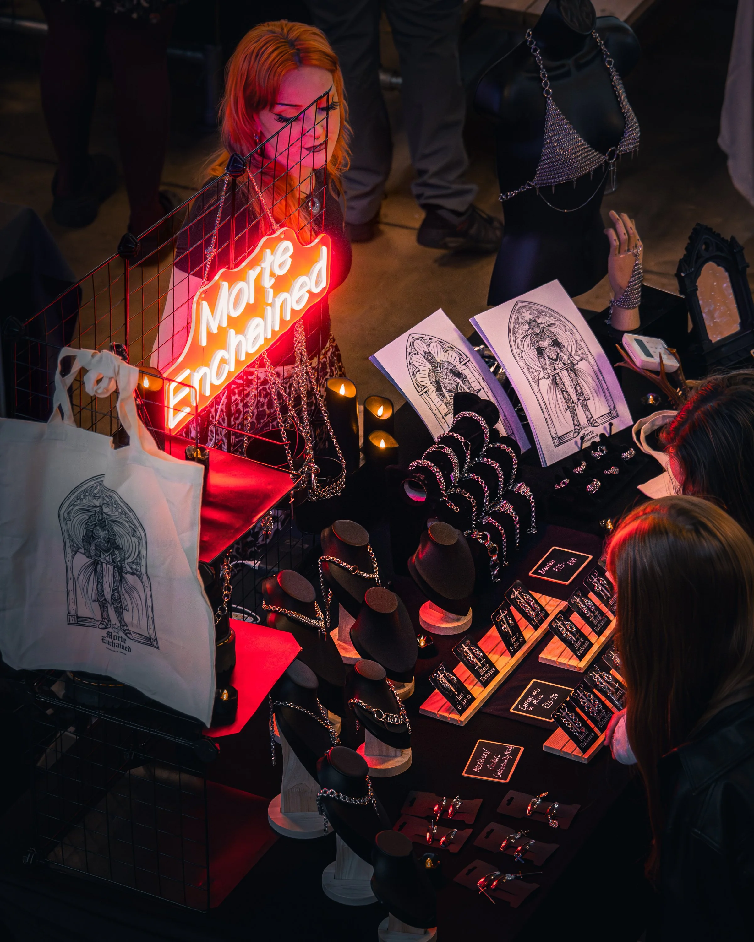 A woman with orange hair at a jewelry stall displaying various necklaces, rings, and jewelry pieces, illuminated by neon signs and display lights.