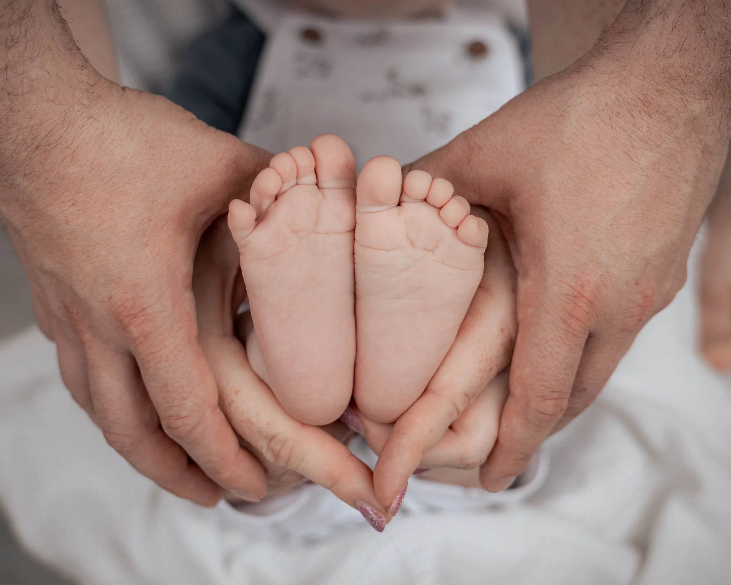 Close-up of an adult's hands forming a heart shape around a baby's feet, which are held gently in the hands.