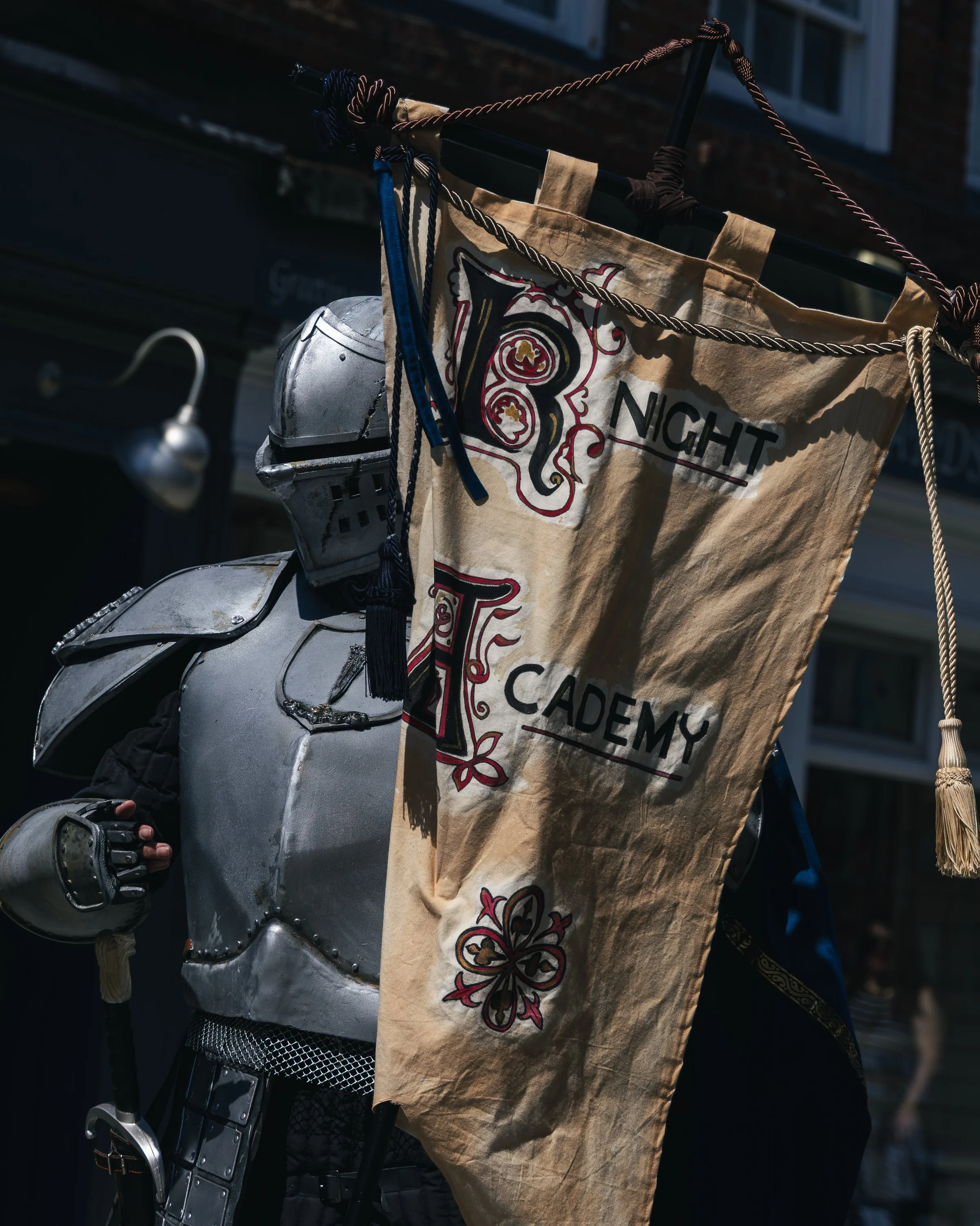 Close-up of a metallic silver motorcycle with a decorative leather bag hanging on the front, displaying an embroidered design with the words 'Night Academy' and ornate patterns.