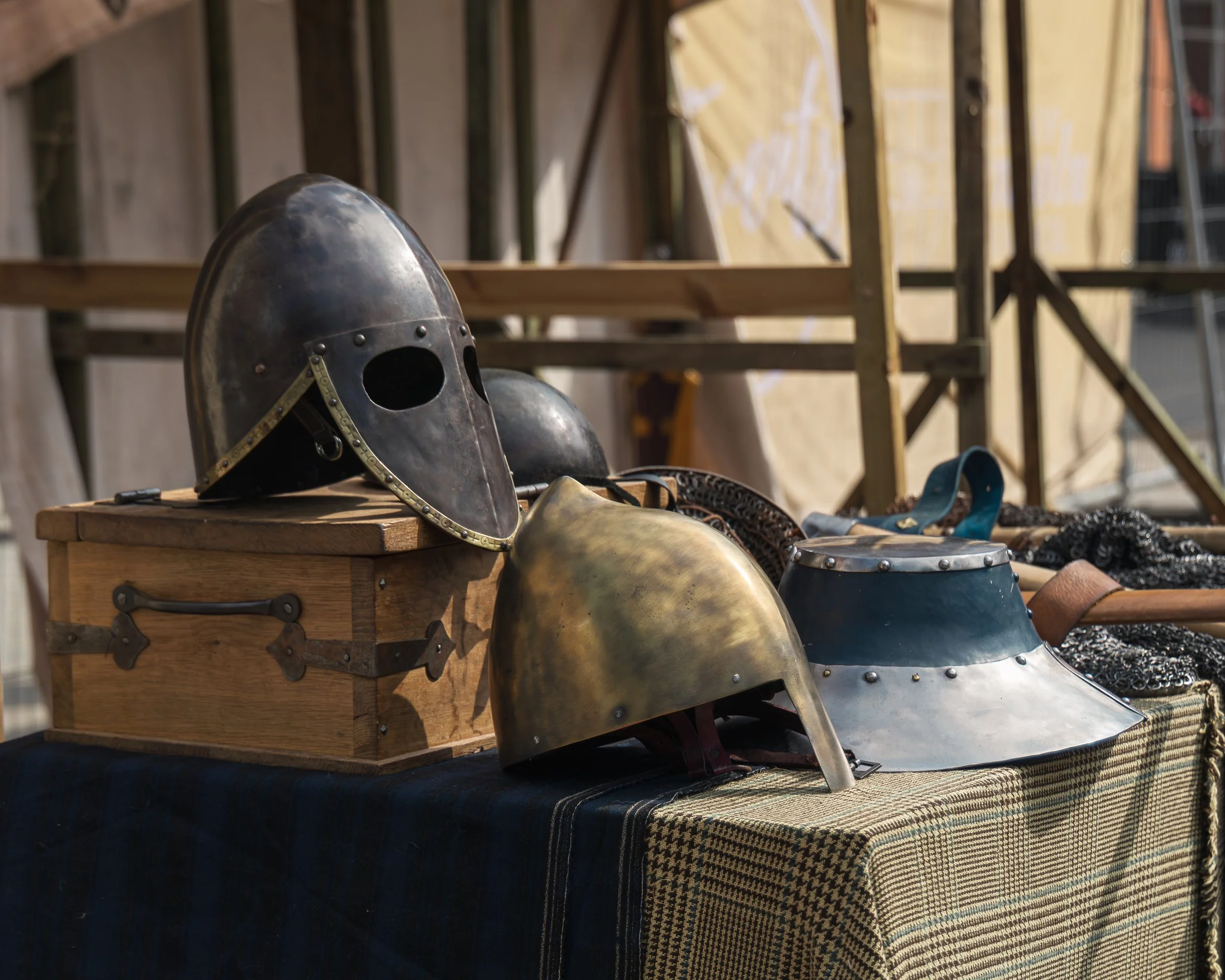 Medieval armor helmets, a chainmail hauberk, and a sword displayed on a wooden table at an outdoor event.
