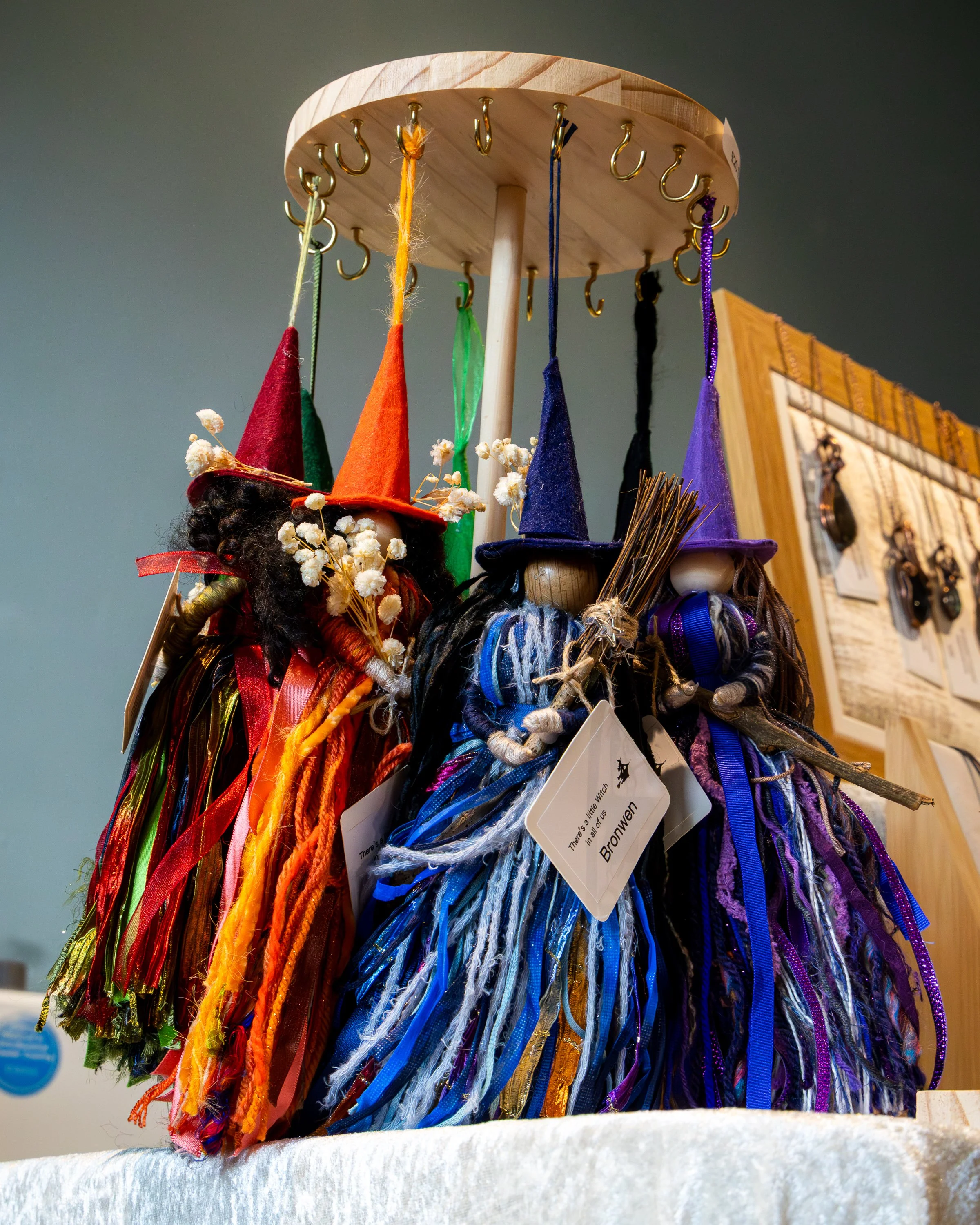 Colorful witch hats on display with various ribbons and yarns hanging from a wooden hat rack.