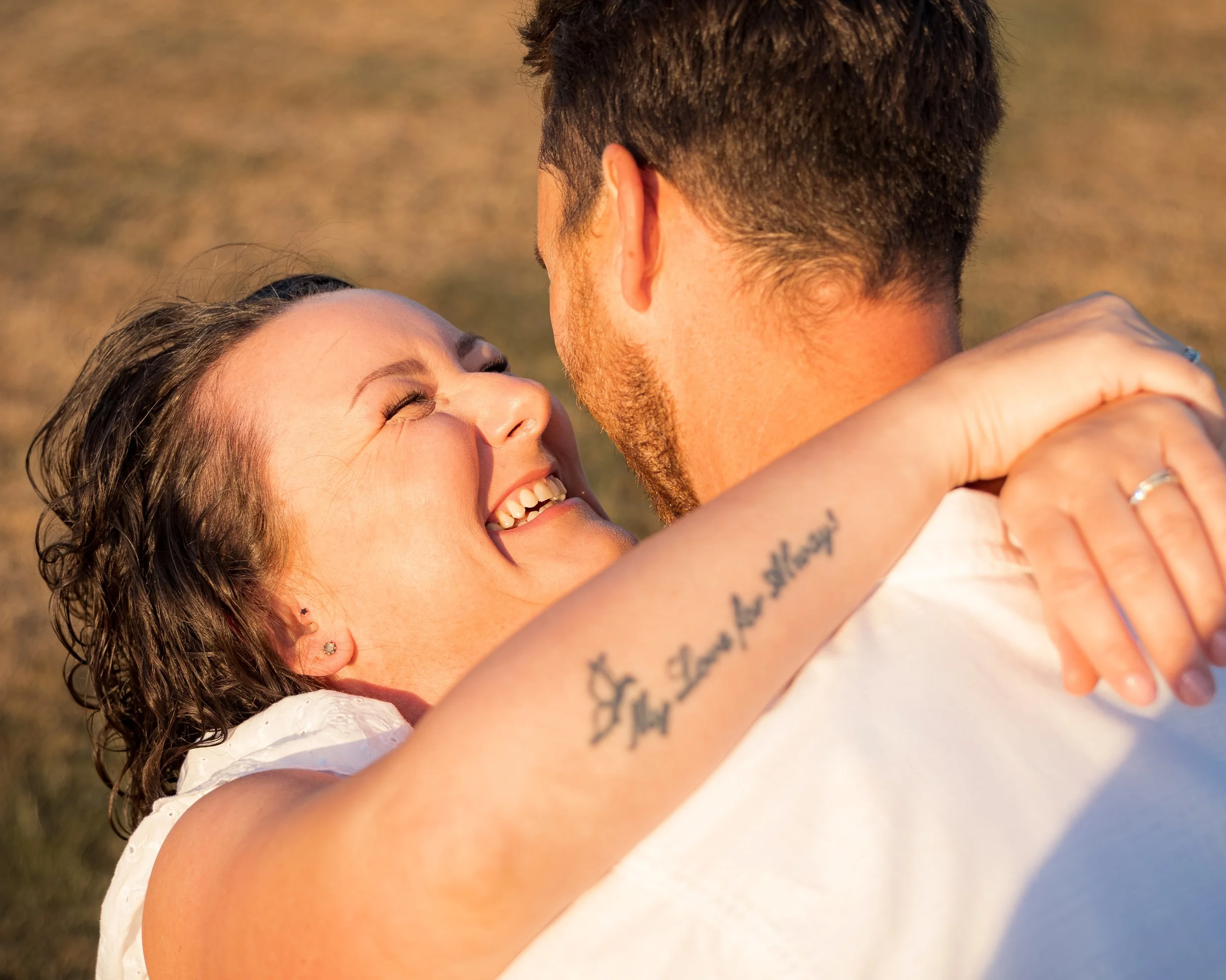 A woman and man are embracing each other, with the woman smiling and the man viewed from behind.