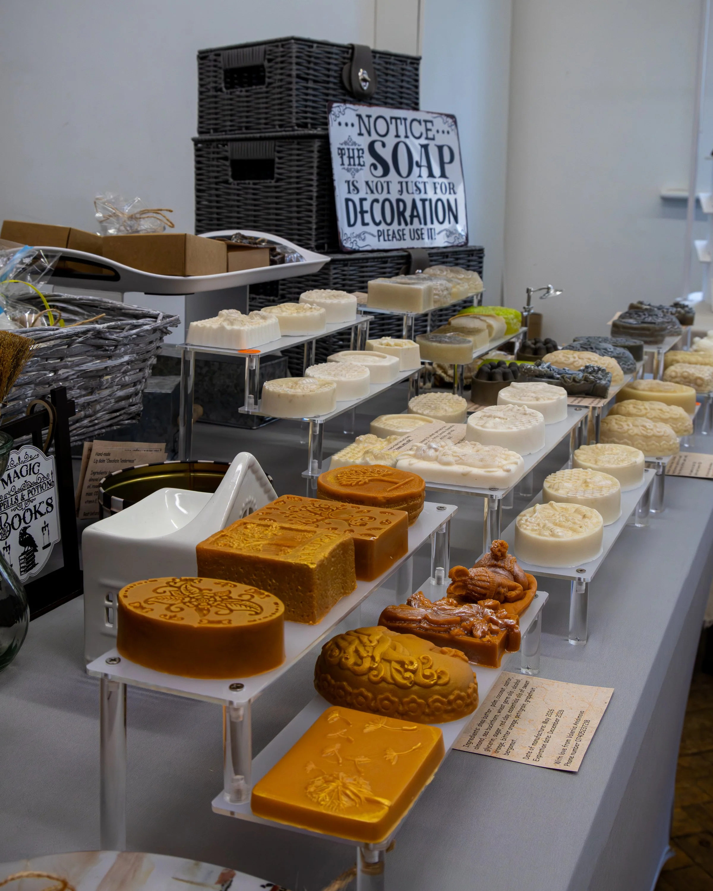 Display of various handcrafted soaps with intricate designs on a tiered white stand, displayed at a market or craft fair.