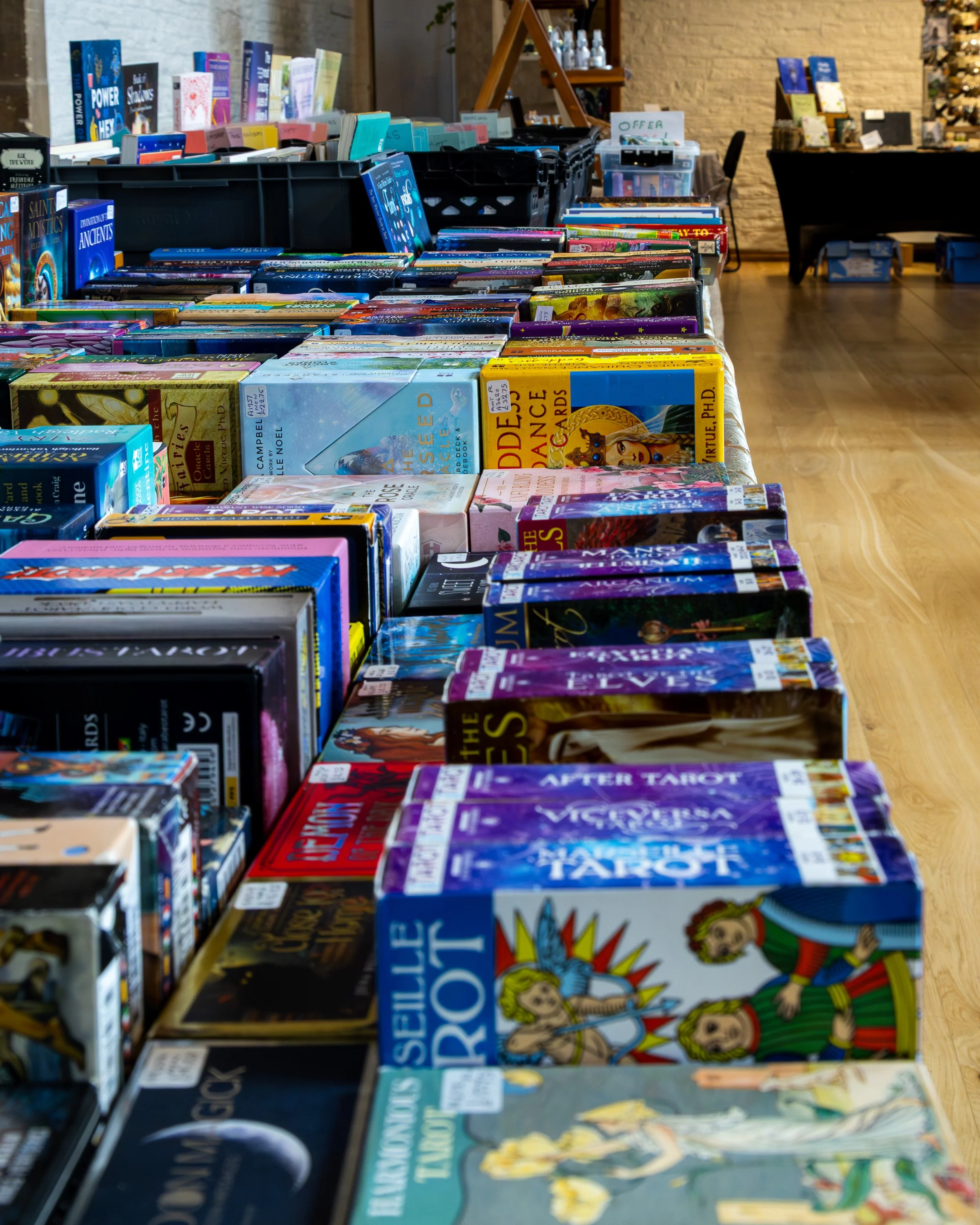 Tables filled with a variety of books arranged in rows at a bookstore or book sale with a brick wall and other tables in the background.