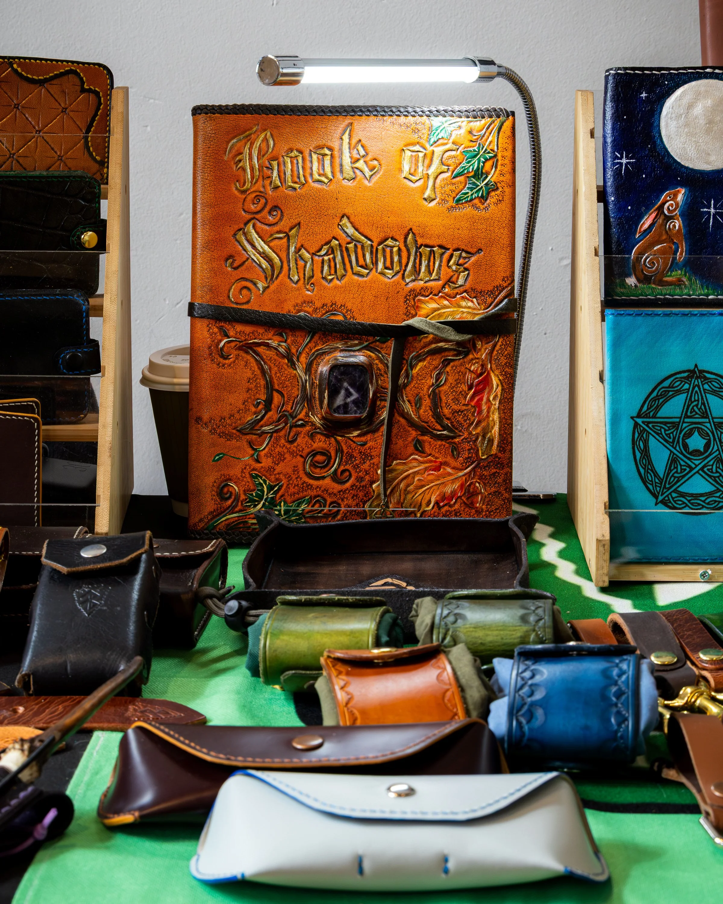Display of leather goods including wallets, pouches, and makeup bags arranged on a green surface at a craft fair or store.