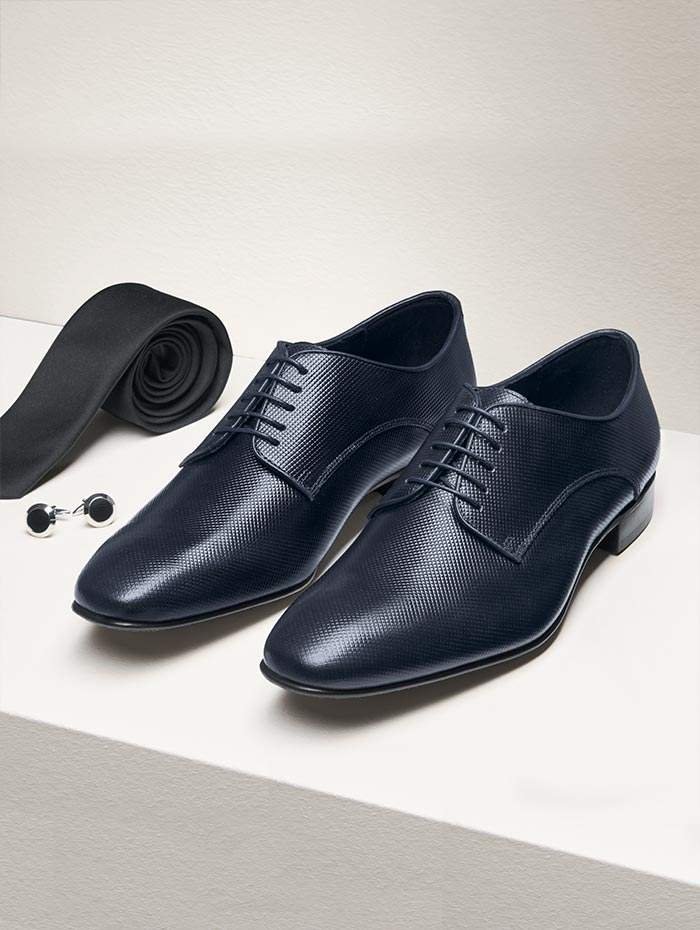 Ein Paar schwarze Lederschuhe, ein schwarzen Gürtel und Manschettenknöpfe auf einer weißen Oberfläche.