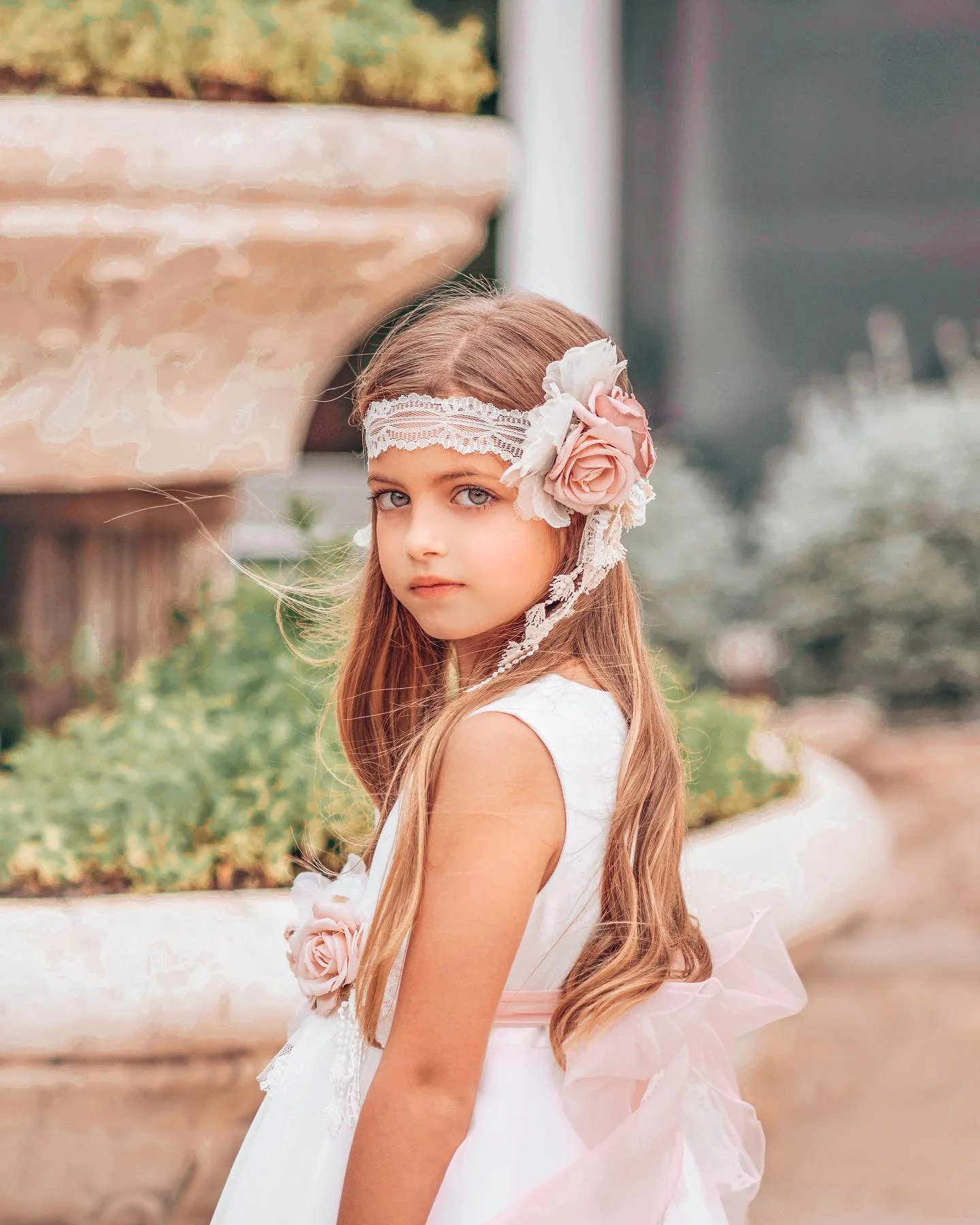 Ein junges Mädchen trägt ein weißes Kleid mit rosa Blumen und einen Haarschmuck mit rosa und weißen Blumen.