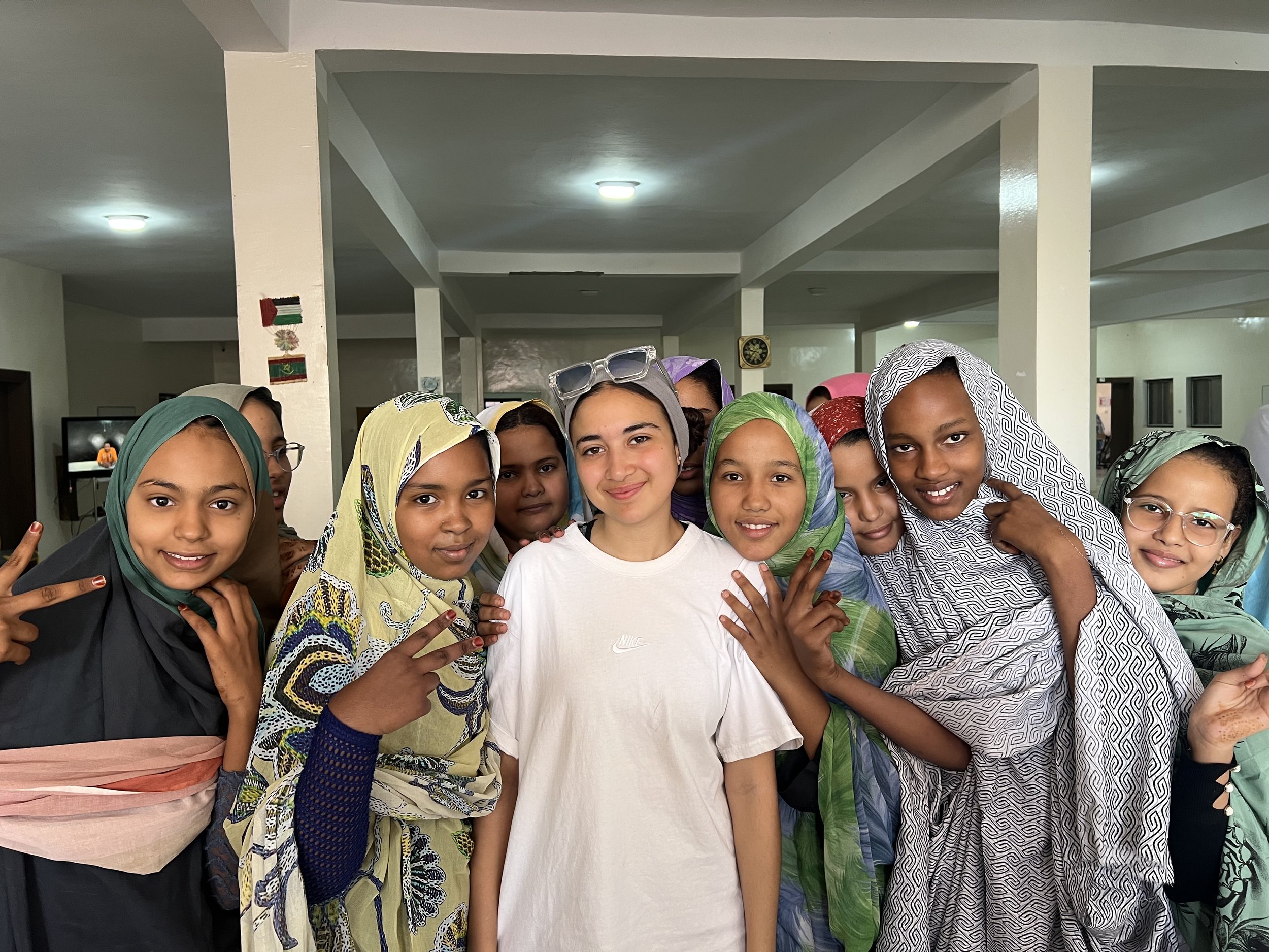 Groupe d'enfants souriants portant des robes colorées et des foulards, posant dans une salle intérieure.