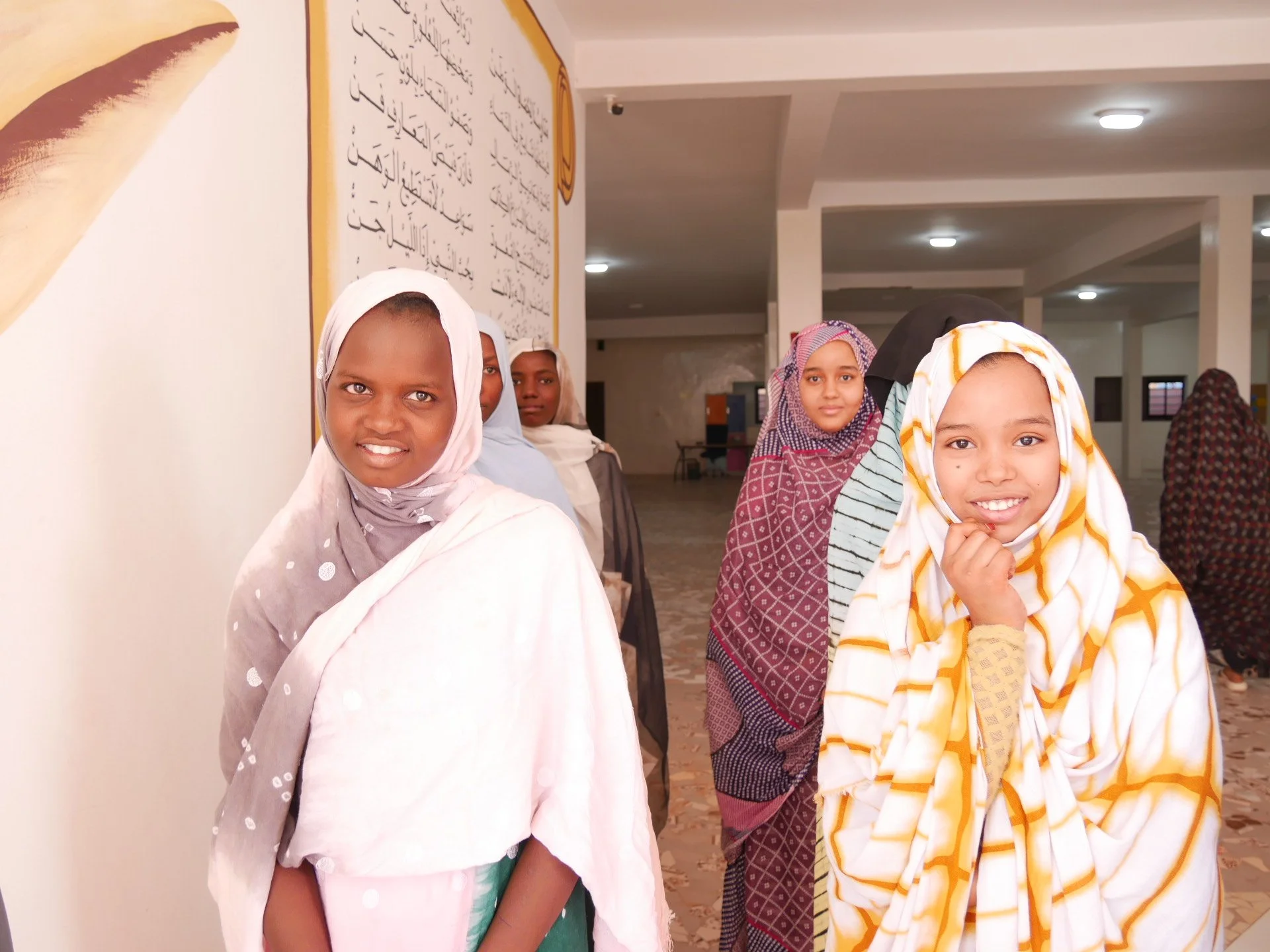 Groupe de jeunes filles portant des hijabs et des vêtements traditionnels dans un intérieur lumineux avec des murs blancs et un plafond éclairé