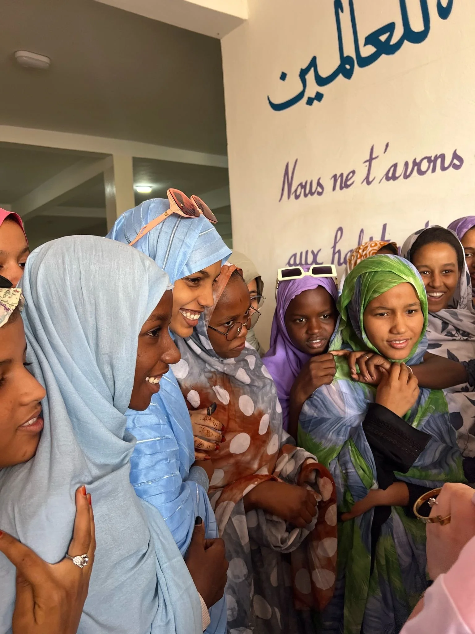 Groupe de femmes portant des foulards colorés, certaines souriant, dans un espace intérieur avec un mur portant un texte en français et en arabe. Le texte en français dit « Nous ne t’avons » et une partie du texte en arabe est visible.