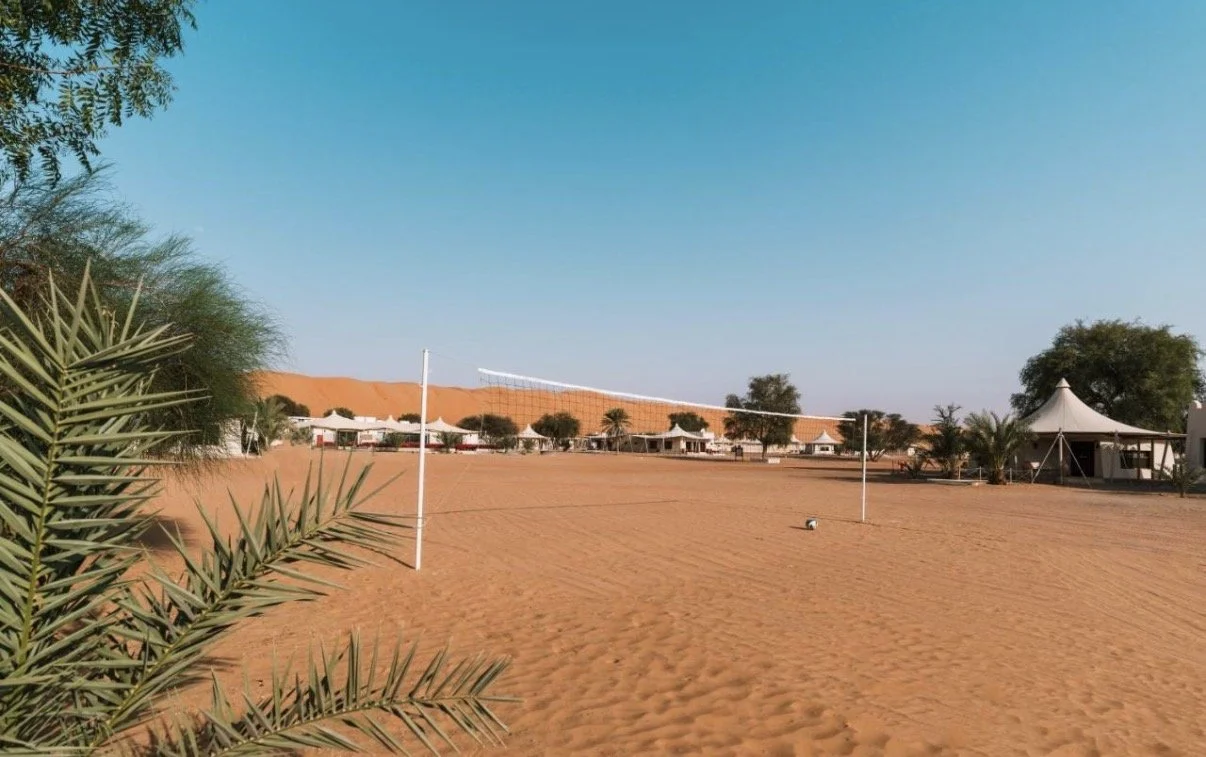 Terrain de volleyball dans un désert avec des tentes et des arbres en arrière-plan.