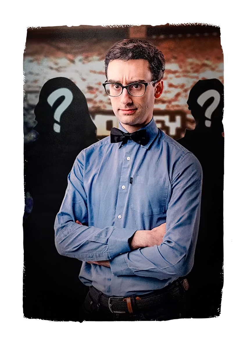 A man with glasses, wearing a blue button-up shirt and a black bow tie, stands with crossed arms against a background featuring two shadowy figures with question marks over their faces, suggesting mystery or unknown persons.