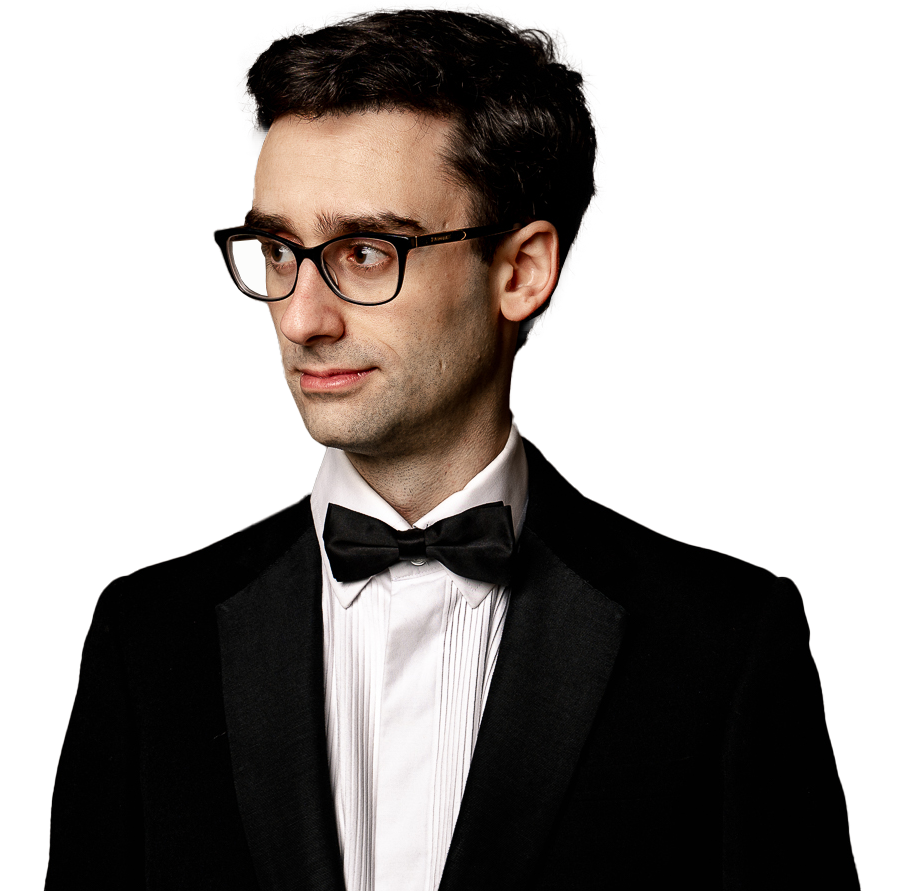 Man in tuxedo with bow tie and glasses looking to the side against a plain background.