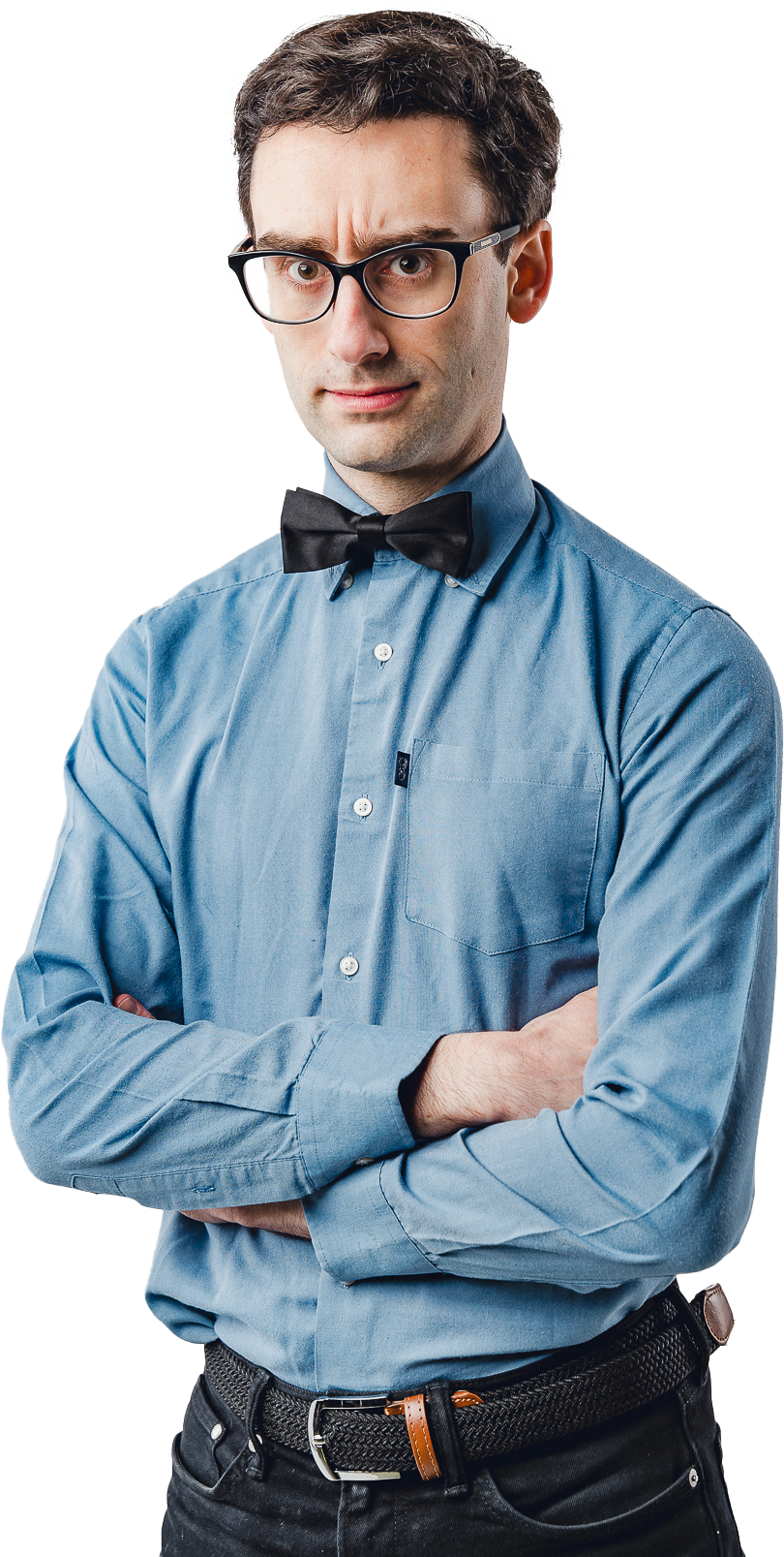 A young man with dark hair, glasses, and light skin standing with arms crossed, wearing a blue button-up shirt, a black bow tie, and black pants, against a plain white background.