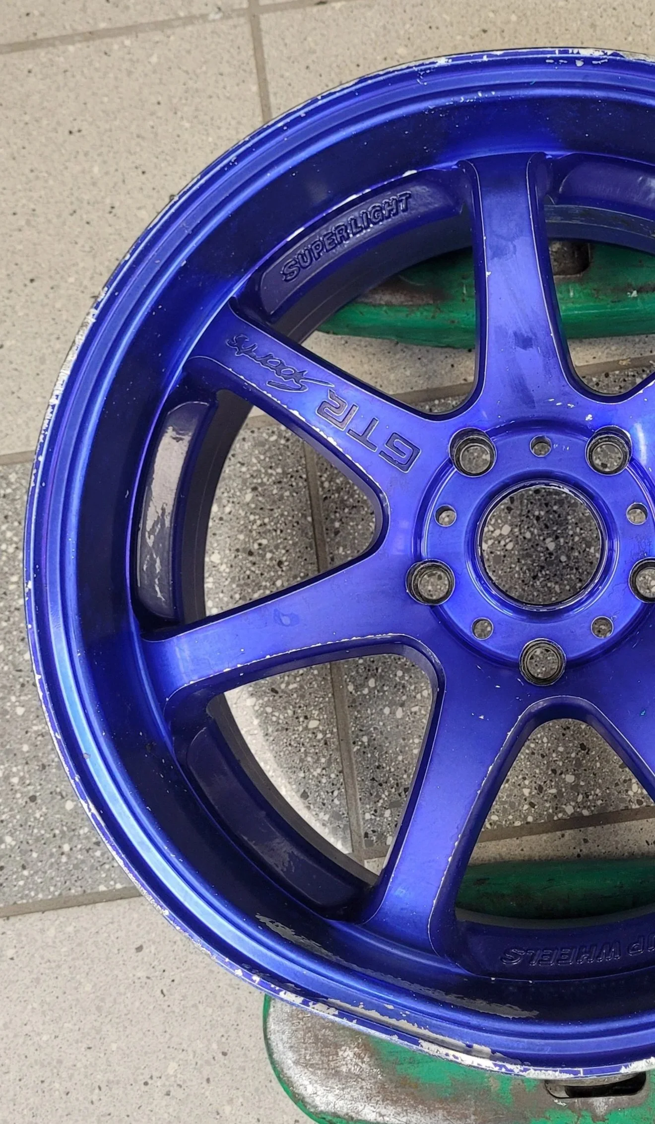 Pneu de voiture bleu avec le mot 'Superlight' écrit, posé sur un sol en carrelage.