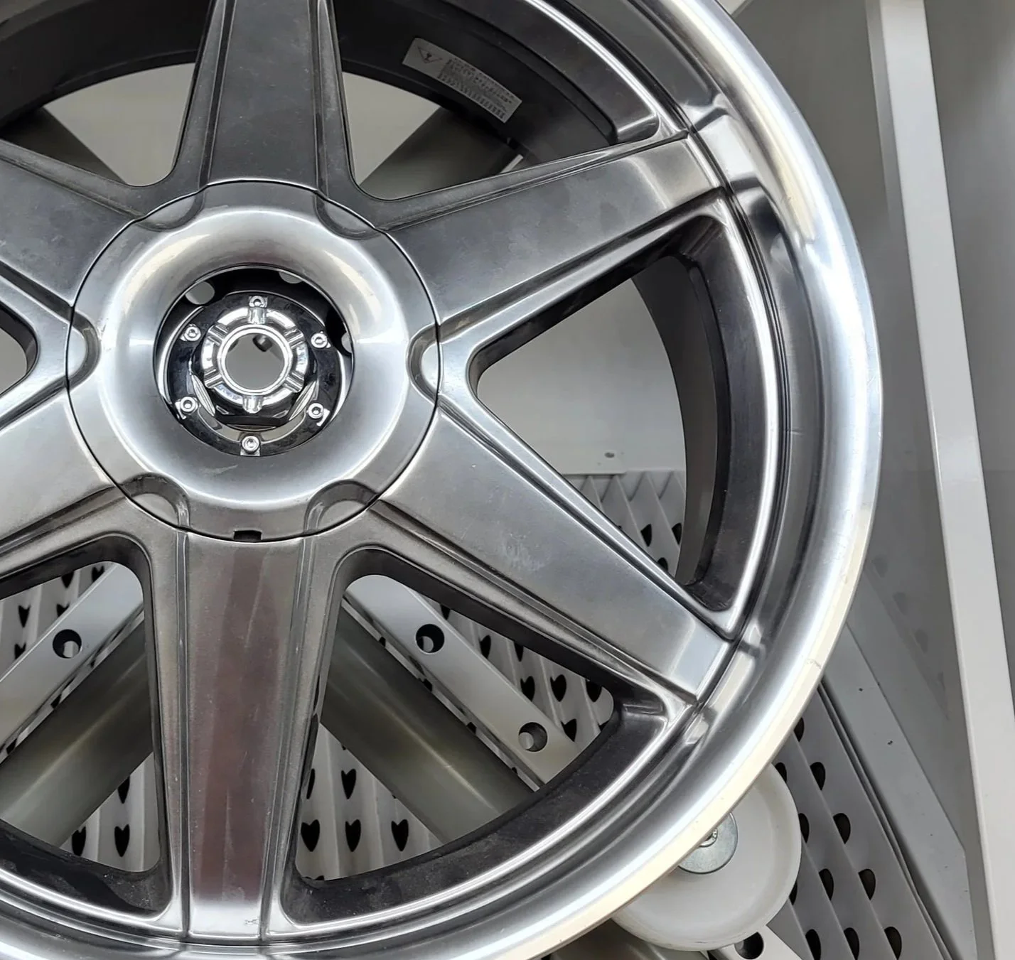 Une roue en alliage légère et brillante, probablement une roue de voiture ou de camion, posée sur un socle, avec un fond de surface perforée.
