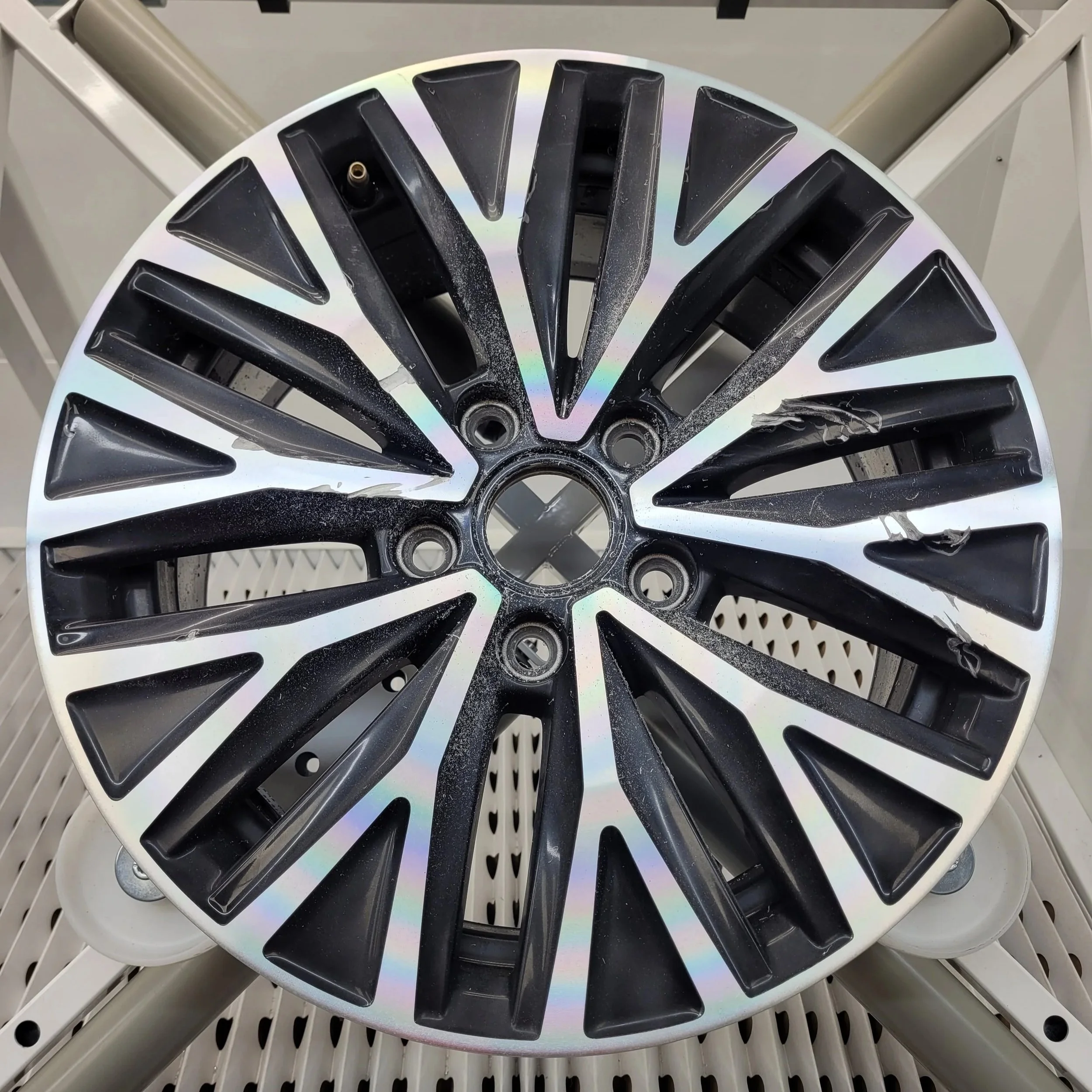 Une roue en alliage à cinq branches noires fixée à un support métallique. La roue est légèrement usée et présente quelques traces de poussière ou de débris.