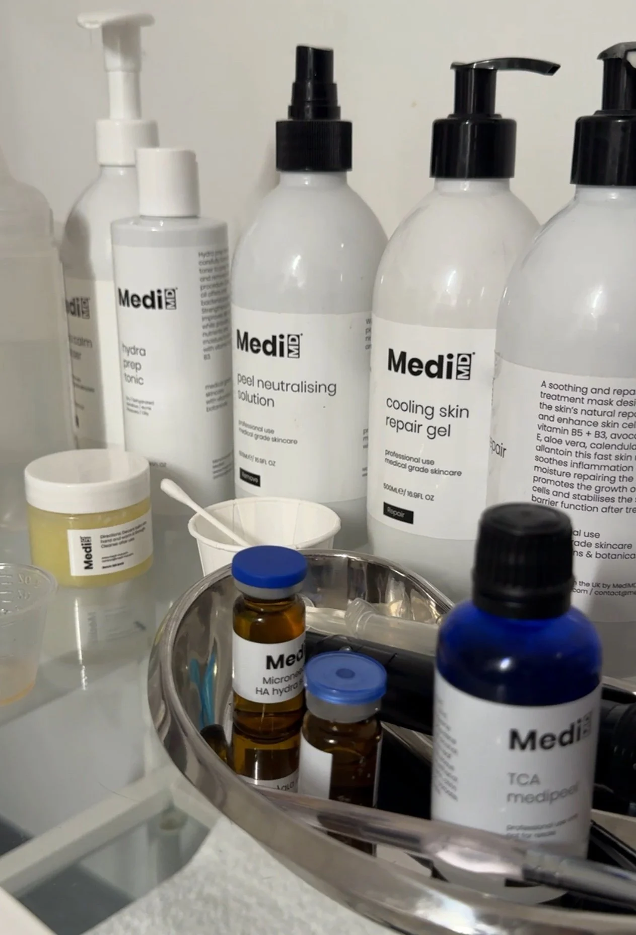 Collection of skincare and medical bottles and containers on a white surface, including MedikMD branded products, in a clinical or medical setting.
